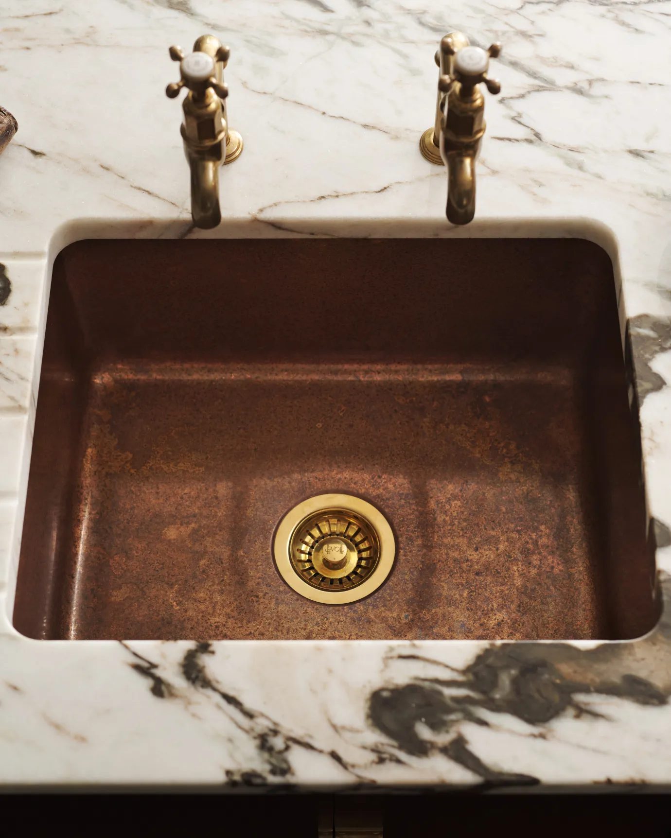 Overhead view of the copper single sink with a patinated finish and brass fittings, set in a white marble worktop with dark veining.