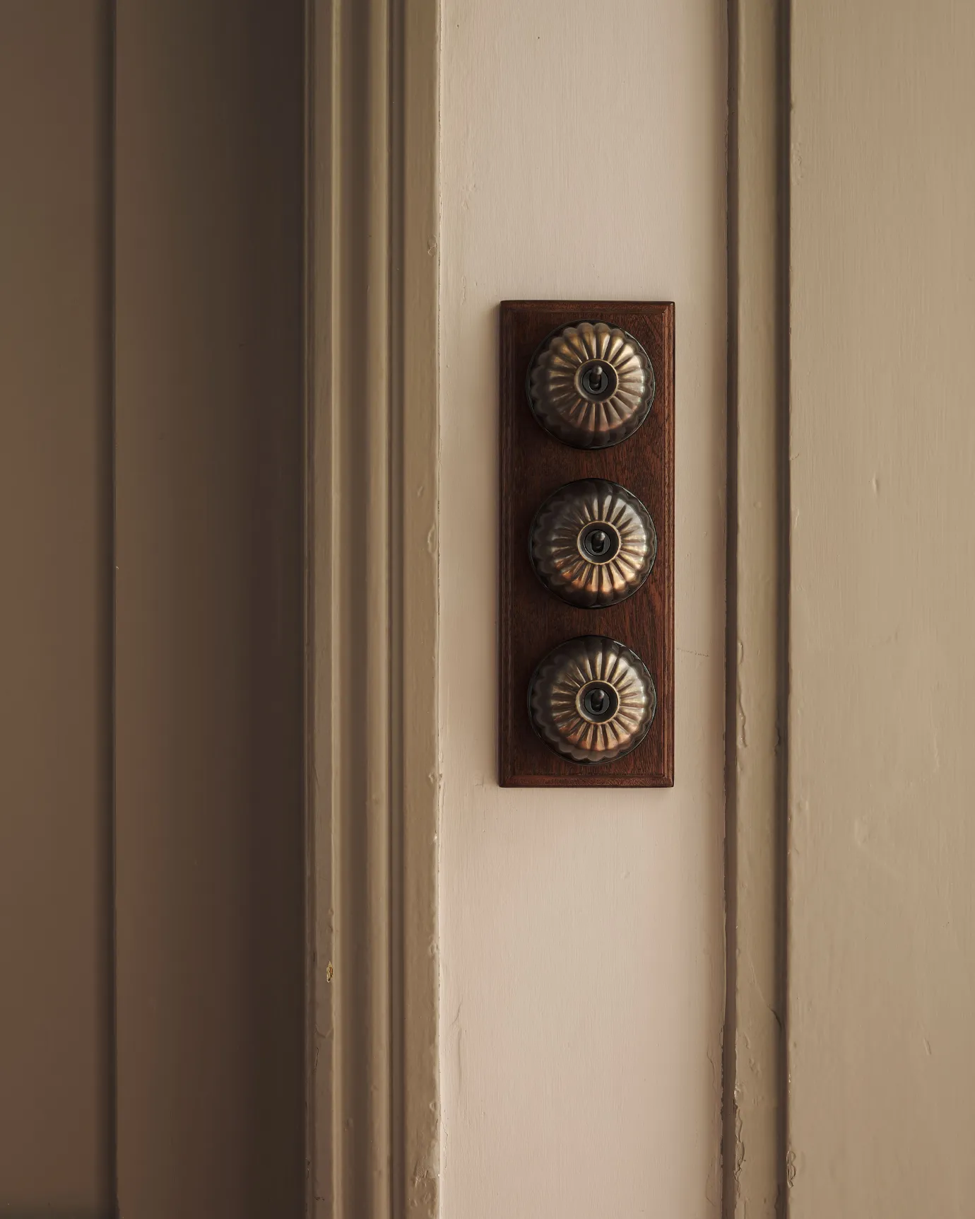 A 3 gang row of Jelly toggle light switches in an Oxidised Brass finish, with black ceramic bases and a Stained Sapele pattress.