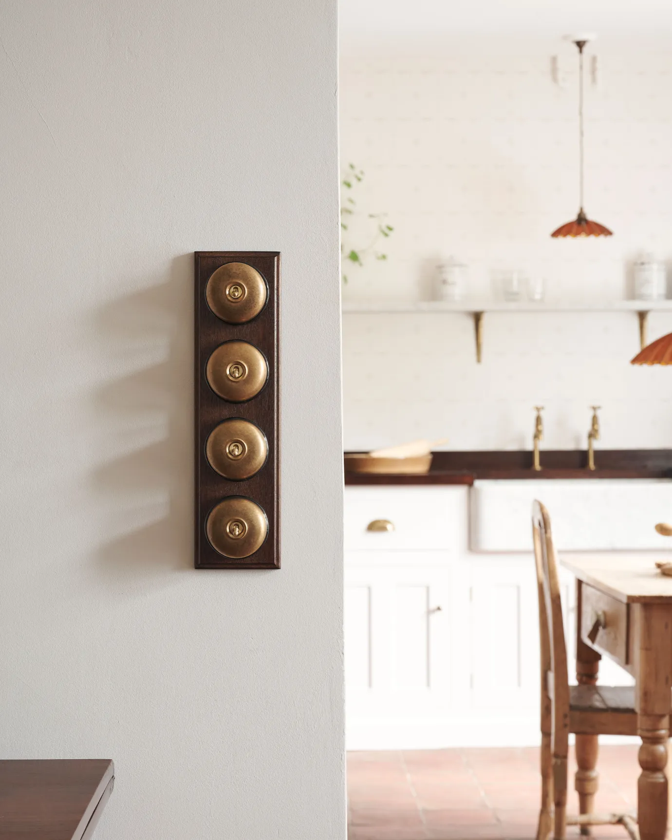 A 4 gang row of Dolly toggle light switches in an Aged Brass finish, with black ceramic bases and a Stained Sapele pattress.