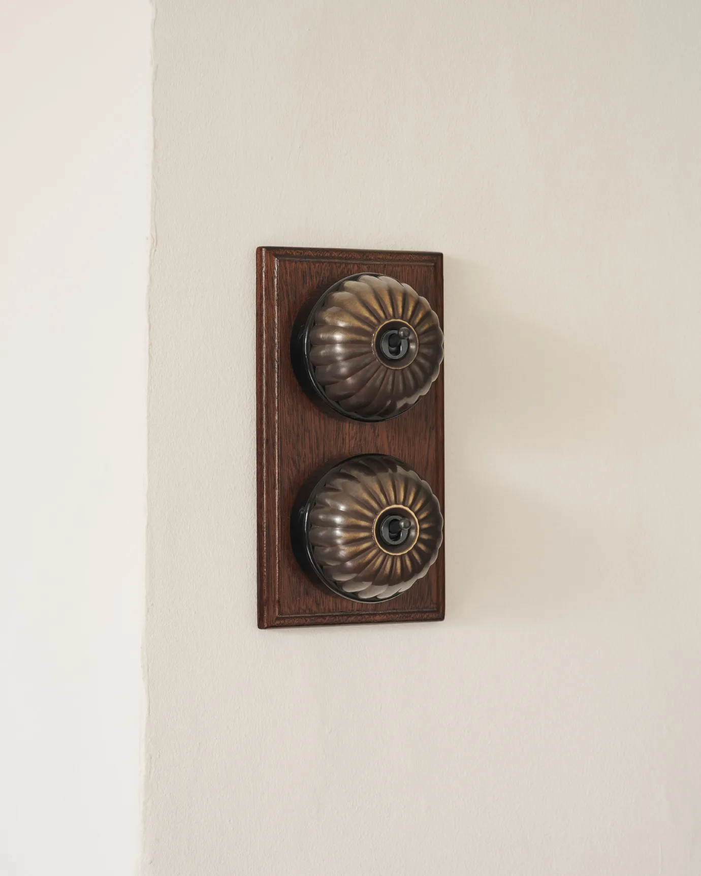 A 2 gang row of Jelly toggle light switches in an Oxidised Brass finish, with black ceramic bases and a Stained Sapele pattress.