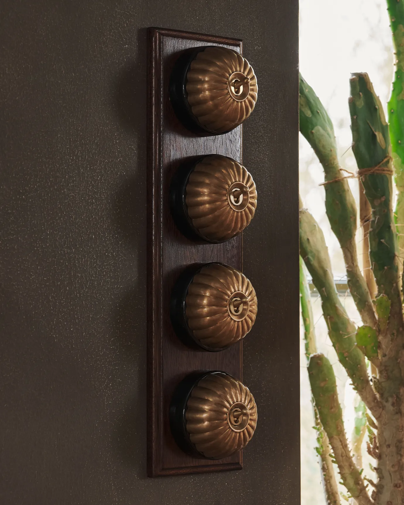 A 4 gang row of Jelly toggle light switches in an Aged Brass finish, with black ceramic bases and a Stained Sapele pattress.