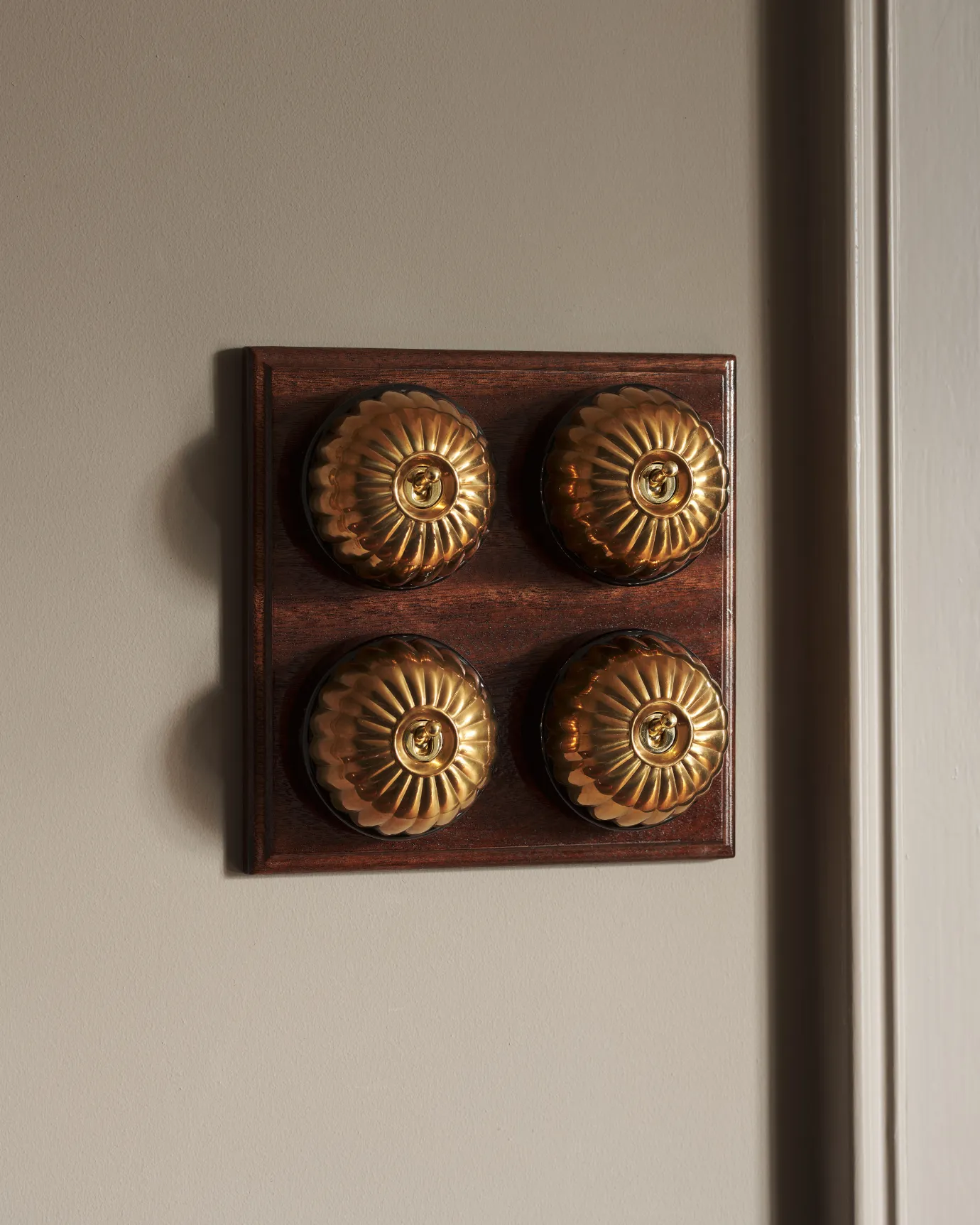A 4 gang bank of Jelly toggle light switches in an Heirloom Brass finish, with black ceramic bases and a Stained Sapele pattress.