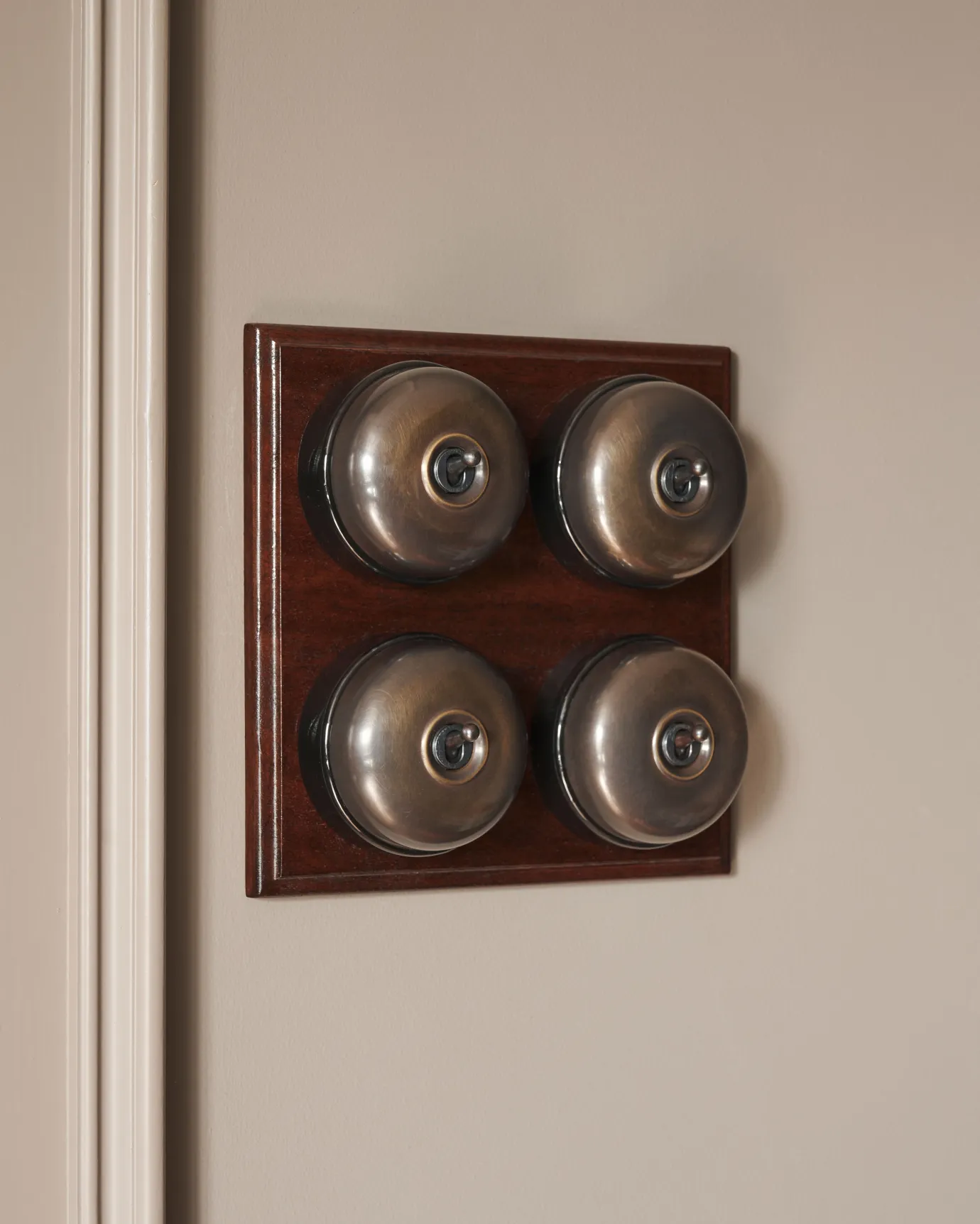 A 4 gang bank of Dolly toggle light switches in an Oxidised Brass finish, with black ceramic bases and a Stained Sapele pattress.