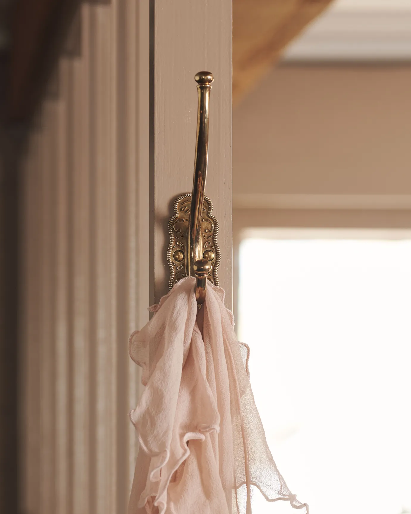 A small Parisian café-style brass hook, fitted to the frame of a pink painted glazed partition.