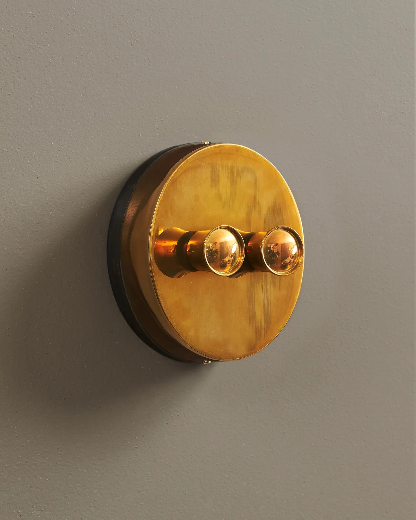 An oblique view of a 2 gang oval-shaped dimmer switch in a warm burnished brass finish with a black base.