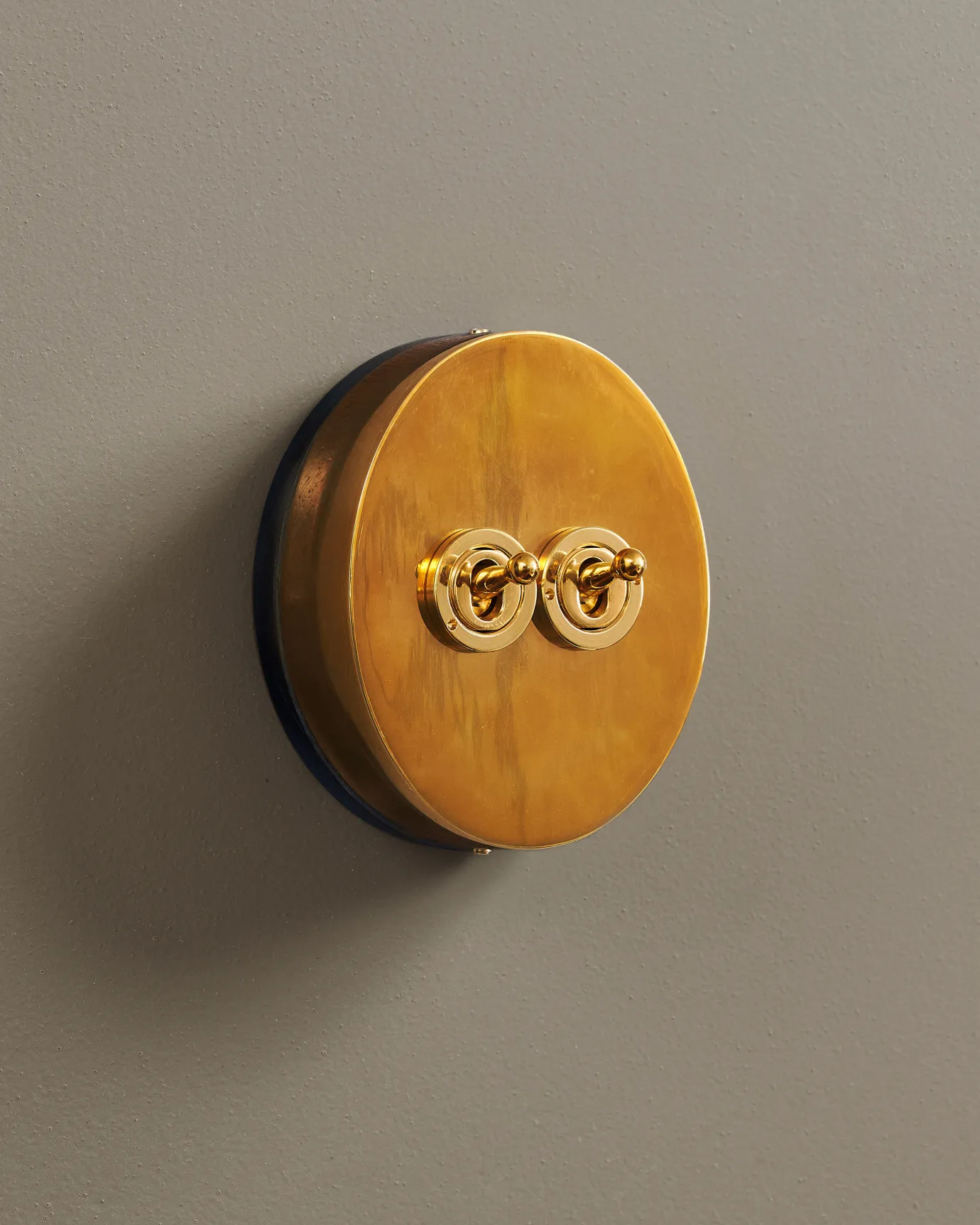 An oblique view of a 2 gang oval-shaped toggle switch in a warm burnished brass finish with a black base.