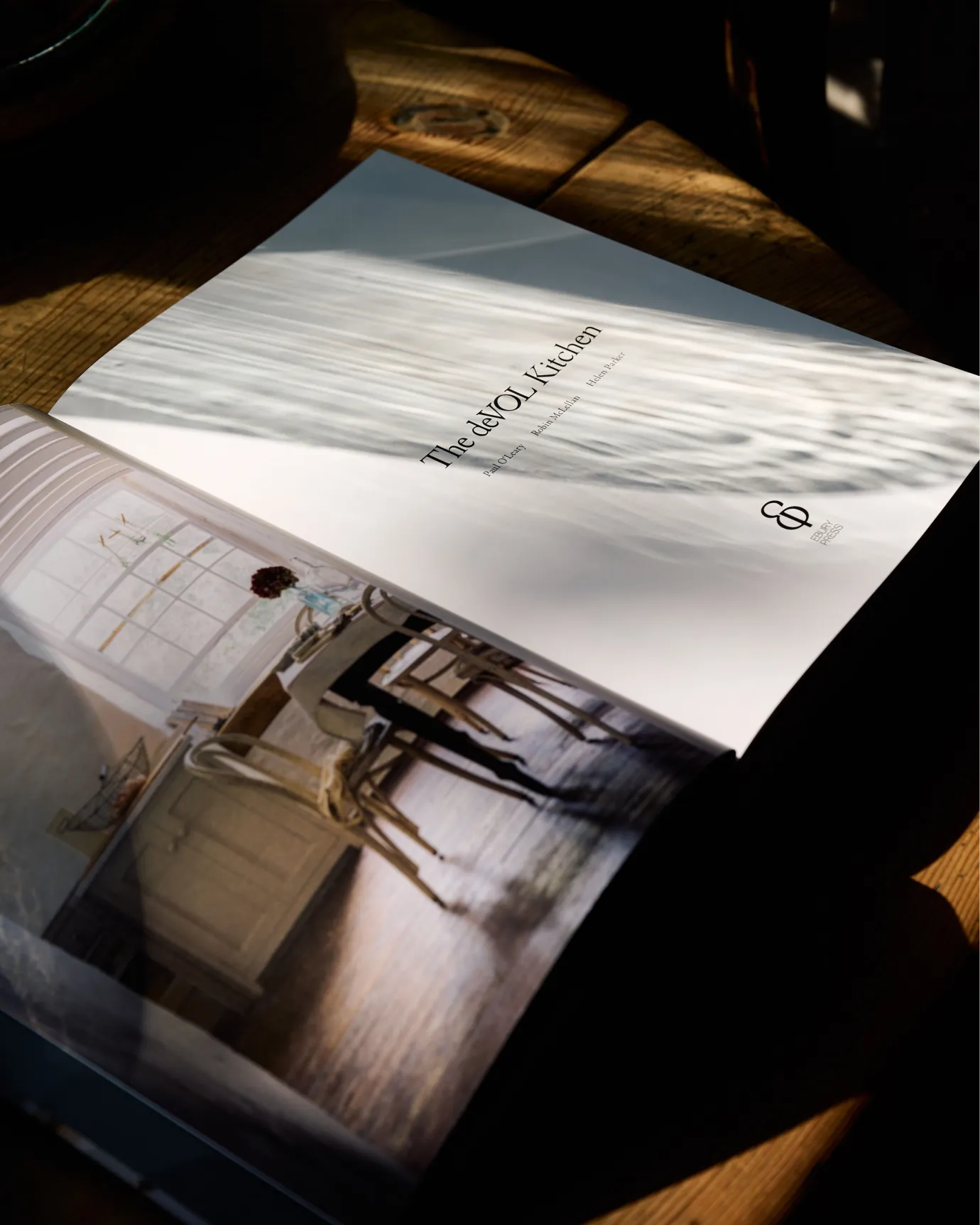 A hardback book open to the first page, showing a photograph of a simple cottage kitchen dining space and the title opposite, 'The deVOL Kitchen'.