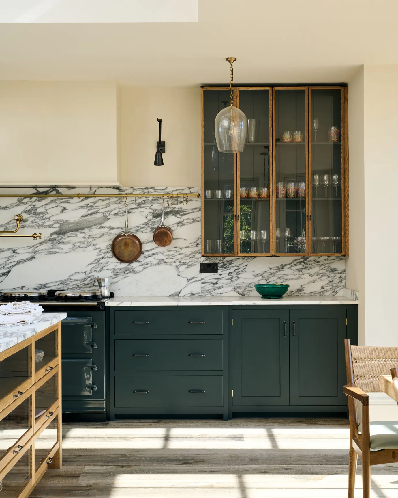 A mid-century-style kitchen with dark green painted base cabinets, a dramatic Arabescato marble splashback and tall glazed wall cupboards with dark interiors.