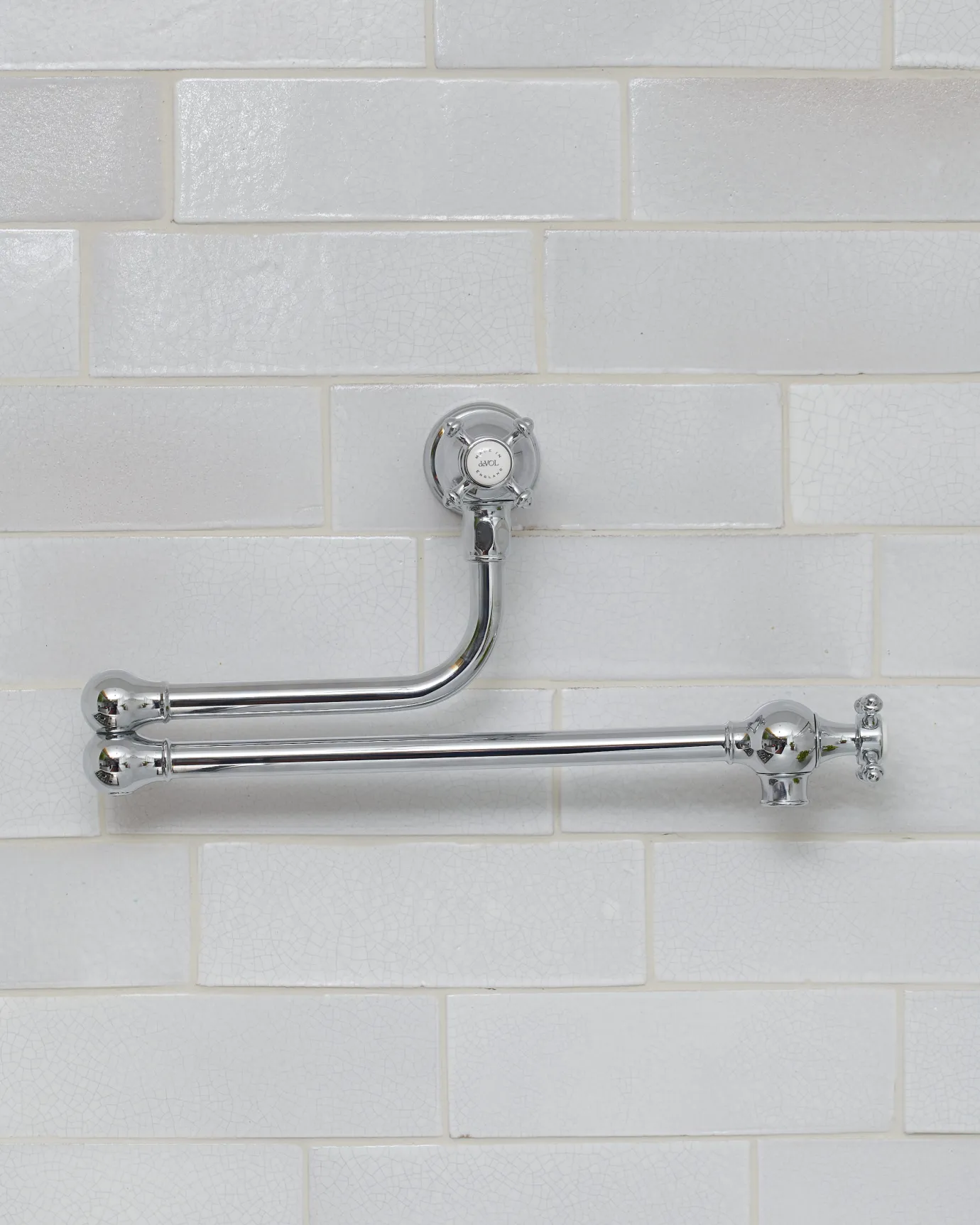 An oblique view of a traditional-style chrome pot filler tap with crosshead handles fitted to a wall of white metro tiles.