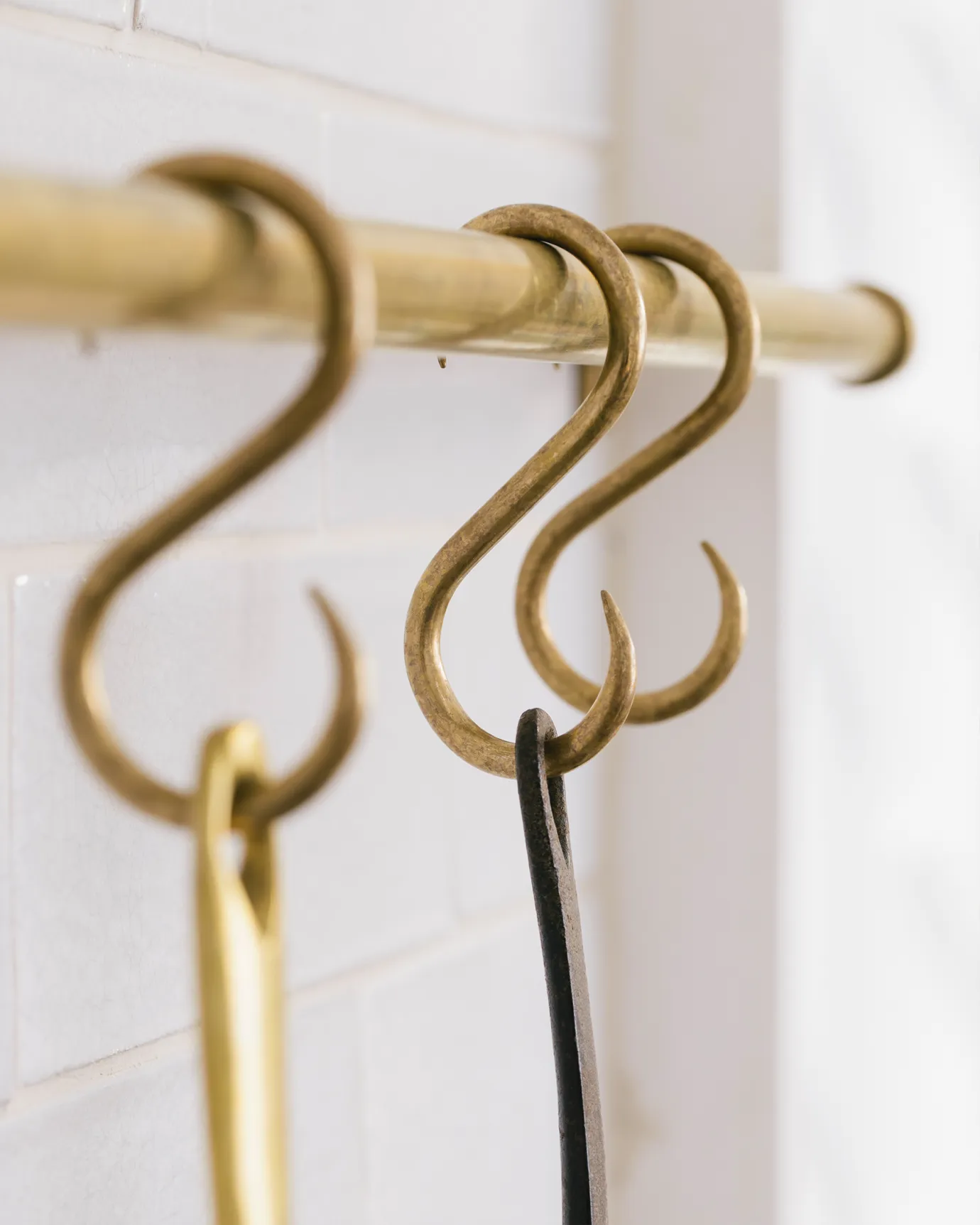 A close-up oblique view of three brass s hooks hanging from an aged brass hanging rail.