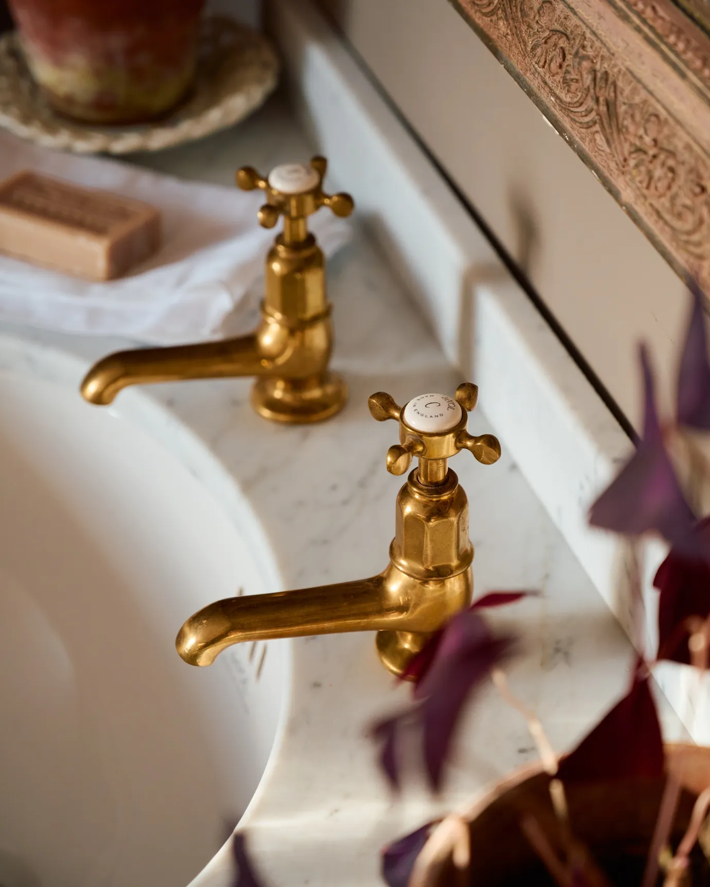 A close-up oblique view of a pair of aged brass pillar taps with crosshead handles for a bathroom basin sink.