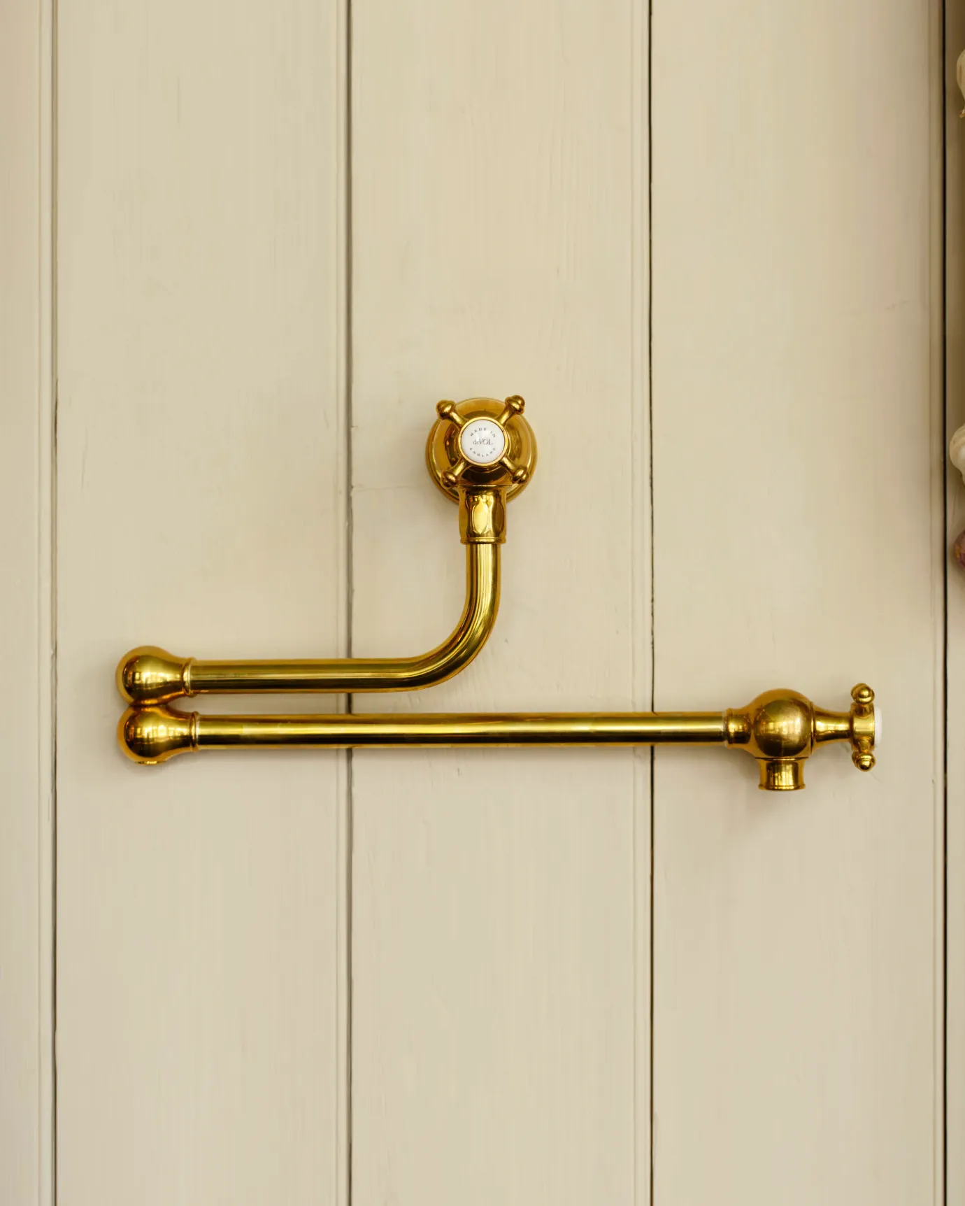 A traditional-style aged brass pot filler tap with crosshead handles fitted to a creamy coloured tongue and groove panelled wall.