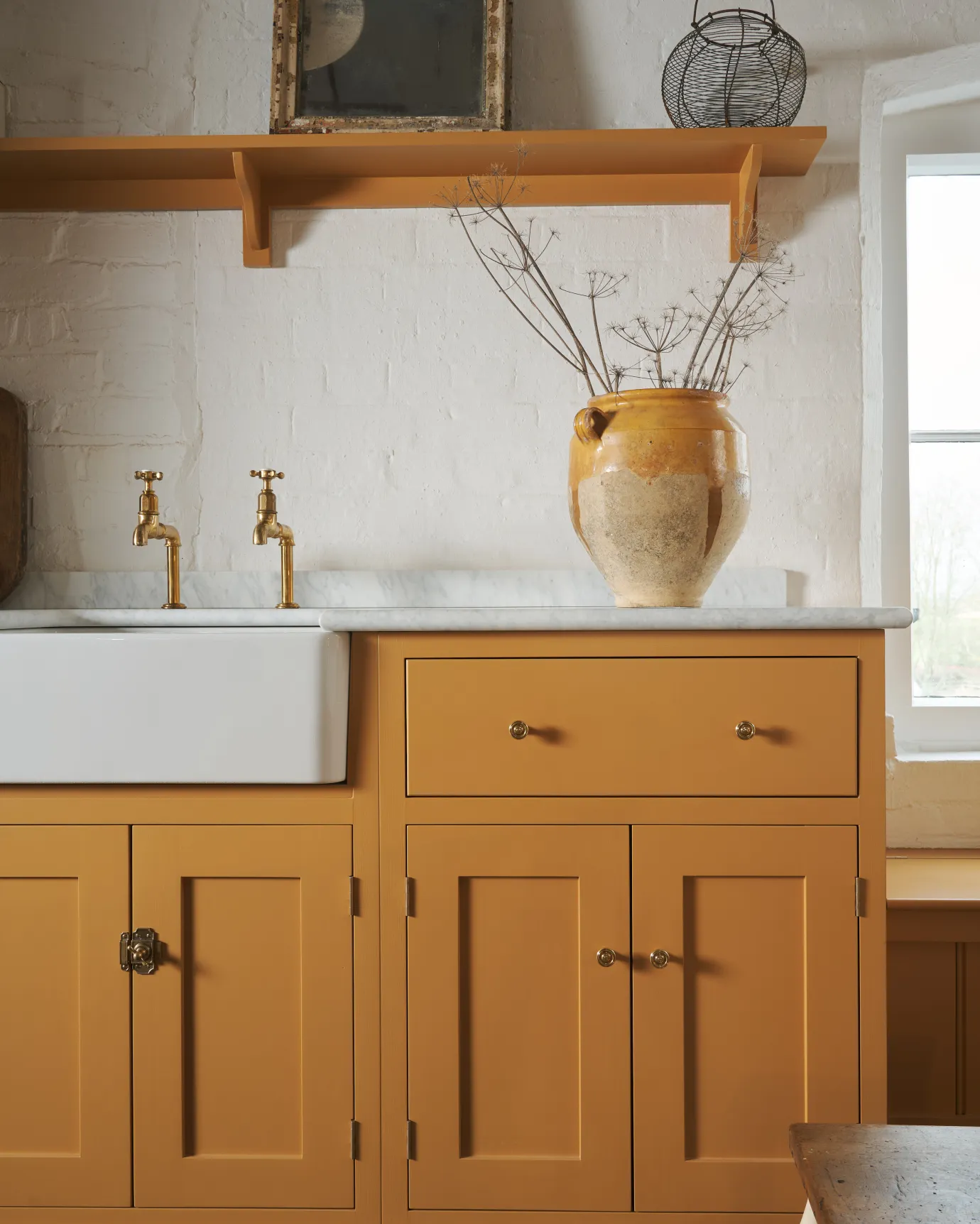 A straight-on view of a yellow painted Shaker-style kitchen sink cupboard with small Victorian-inspired doorknobs in a warm burnished brass finish.