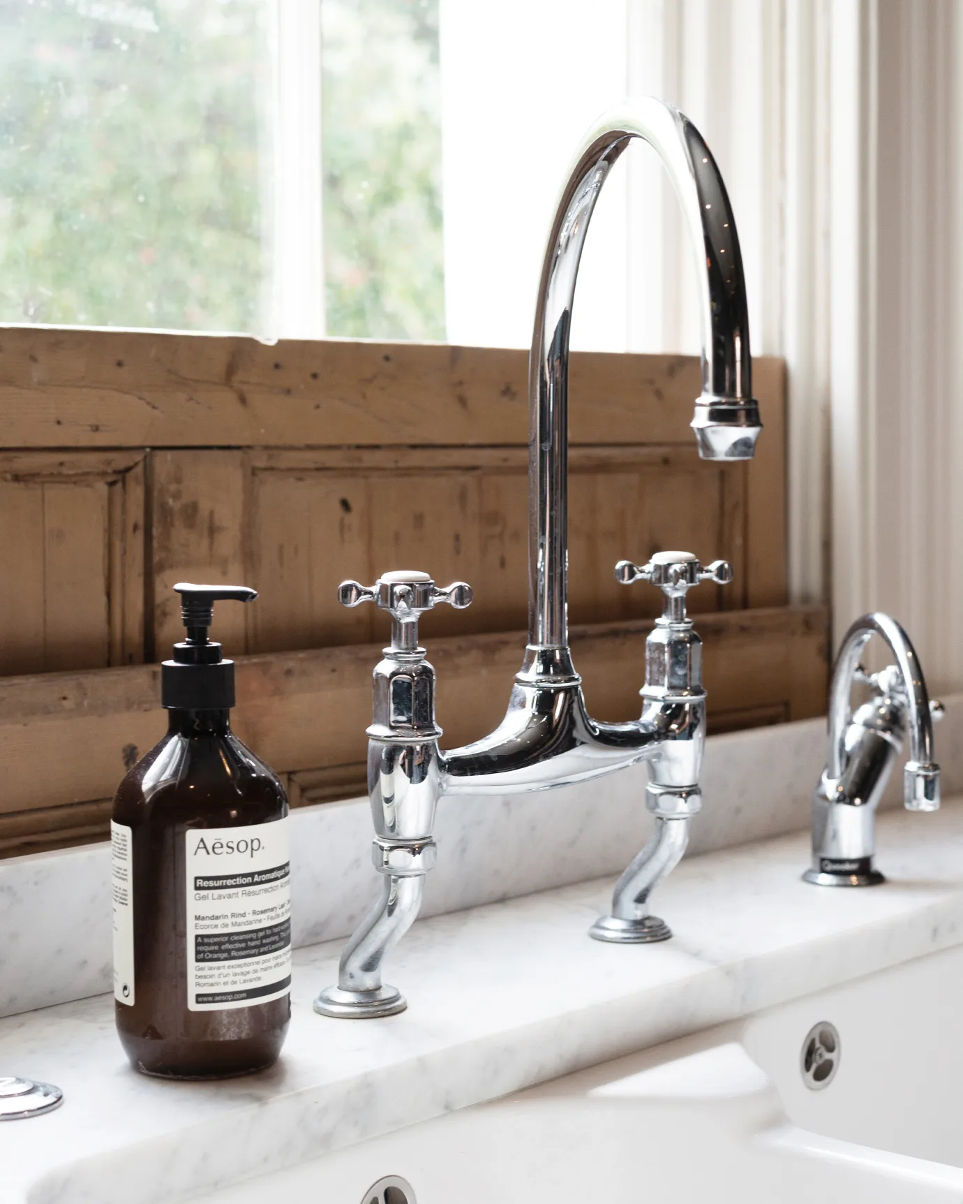 An oblique view of a traditional-style chrome mixer tap with crosshead handles with traditional pine shutters behind.