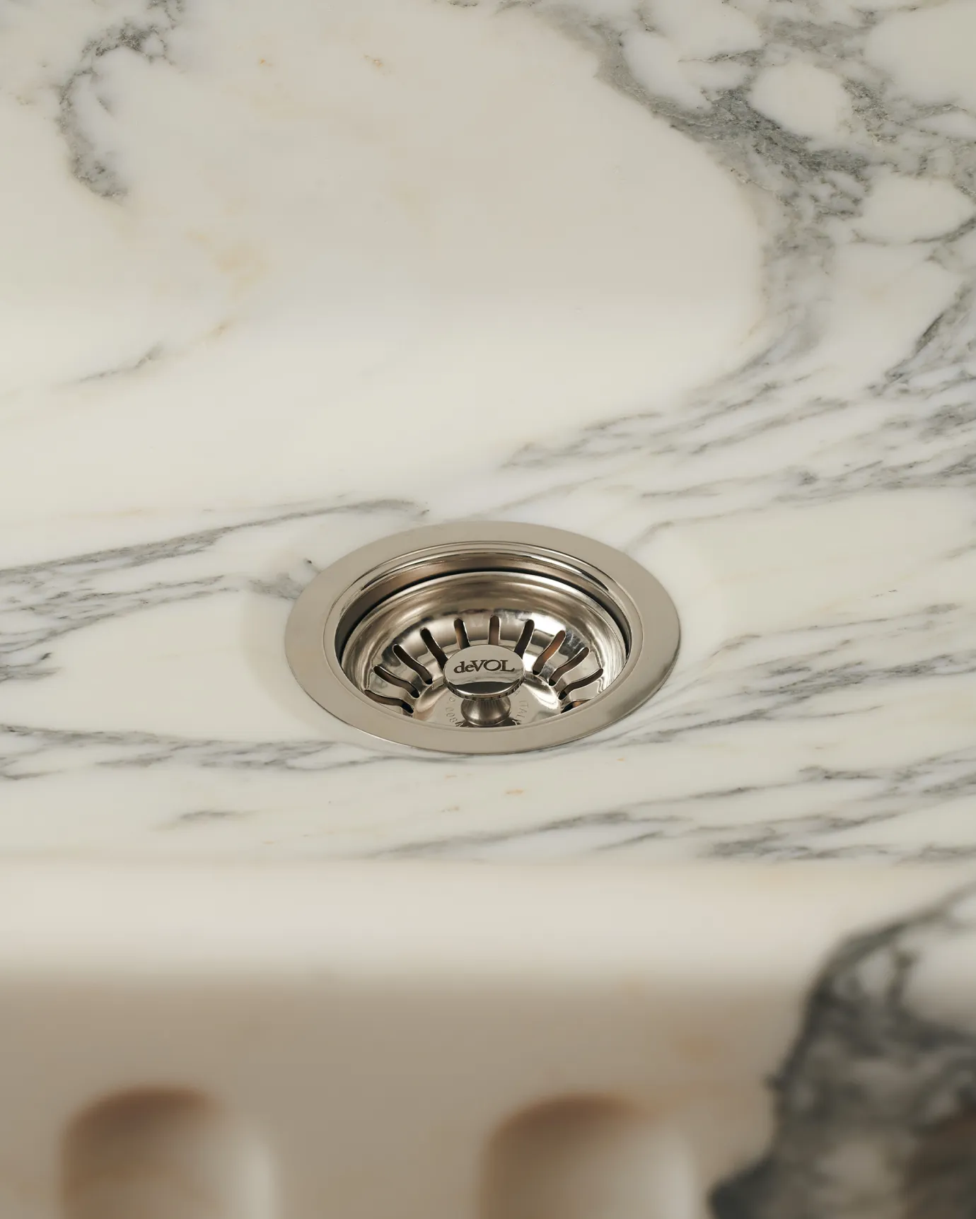 A straight-on view of a basket waste strainer in a polished chrome finish fitted in an Arabescato marble sink.