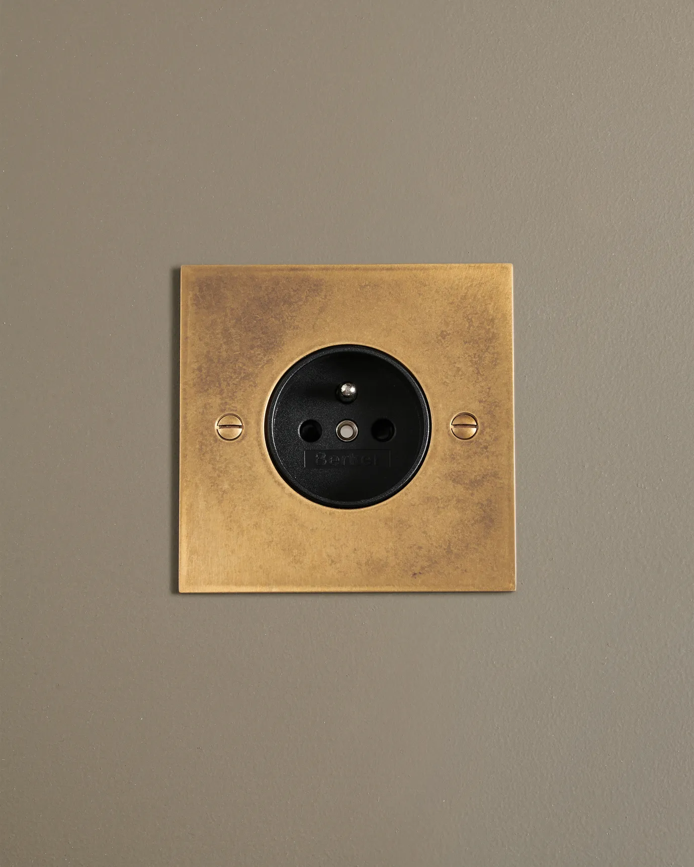 A straight-on view of a classic French-style single plug socket in a mottled aged brass finish.