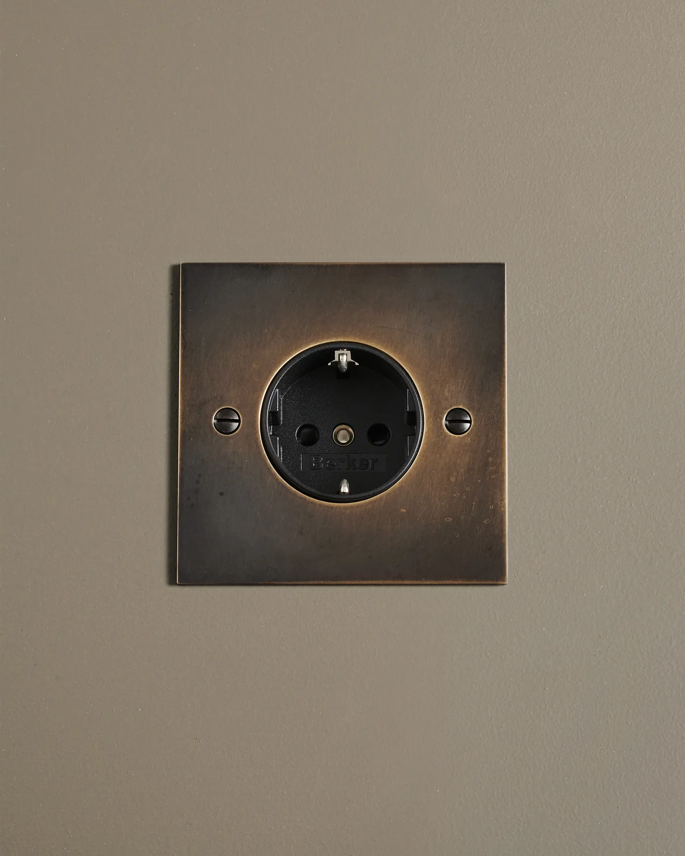A straight-on view of a classic Schuko-style single plug socket in a dark oxidised brass finish.