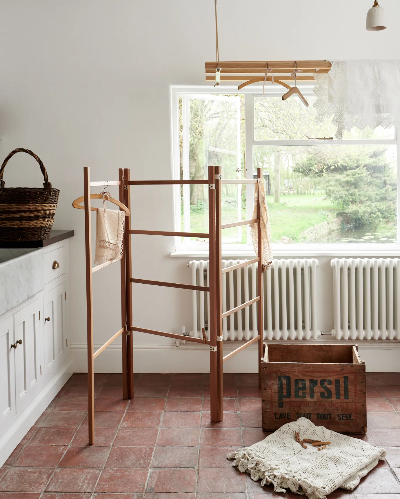 A wooden clothes horse in a Mediterranean-inspired room with white walls, terracotta flooring and rustic styling.