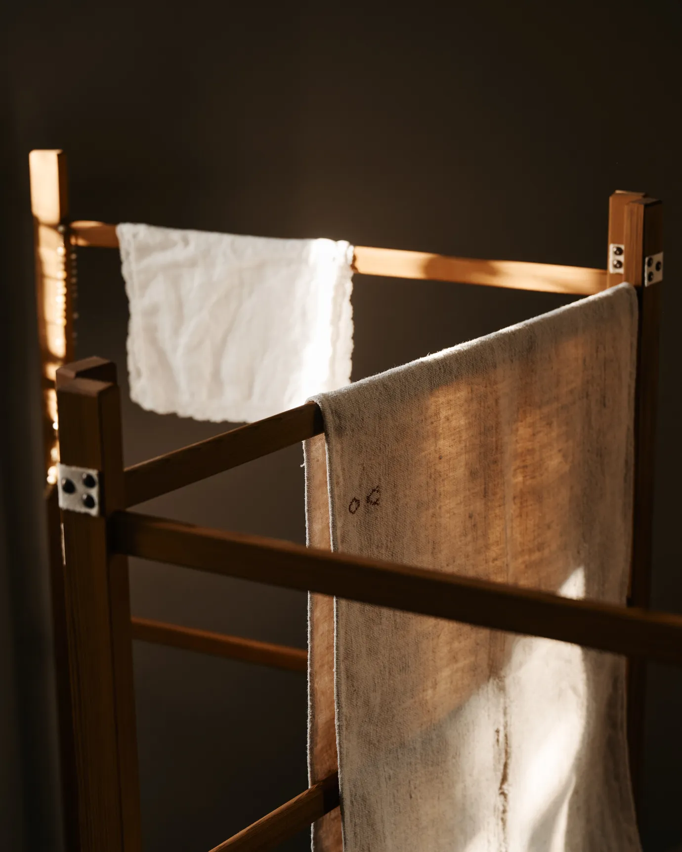 A wooden clothes horse with vintage linen towels draped over it, in a dark room.