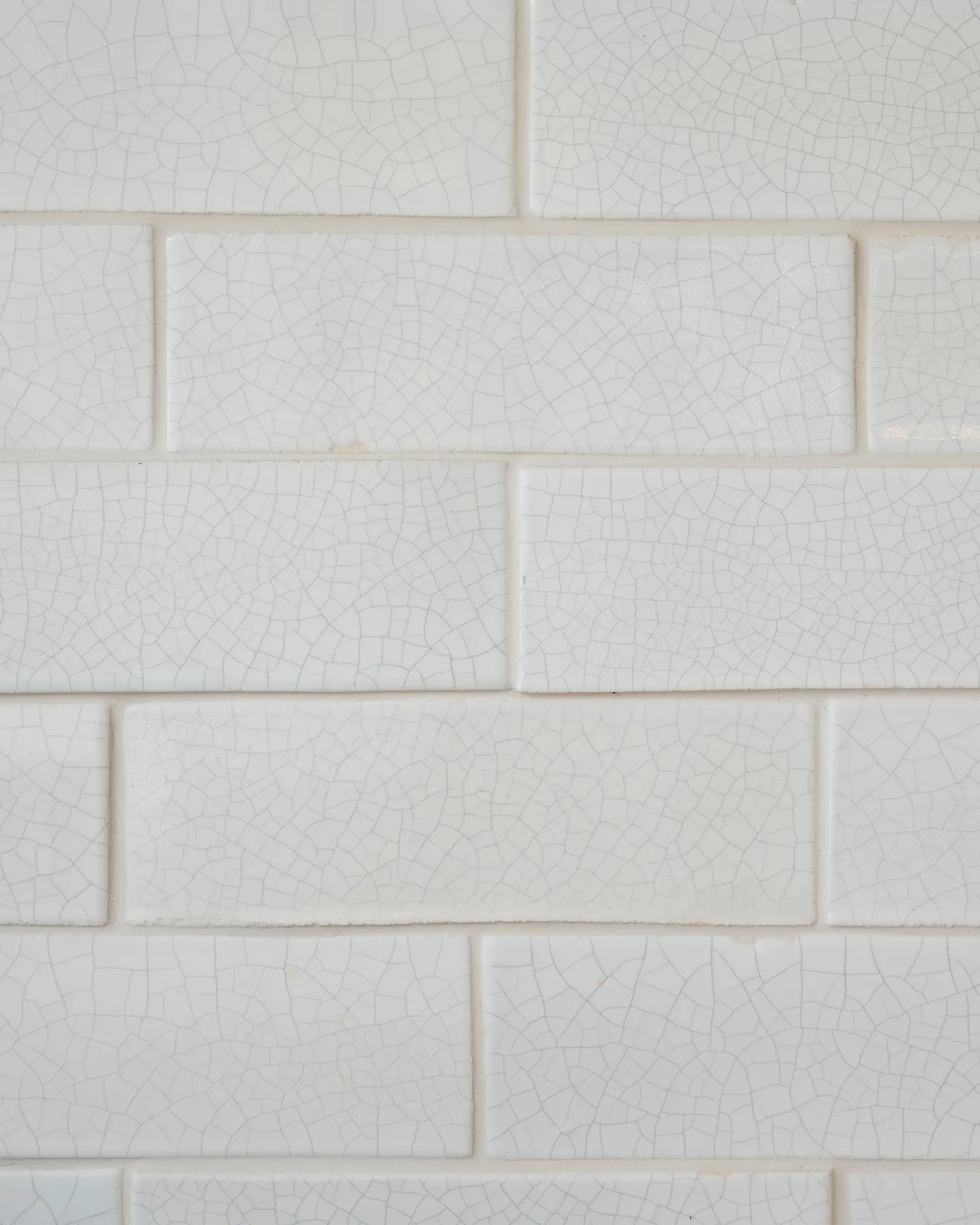 A close-up view of glossy white metro wall tiles with delicate charcoal crazing across the surface.