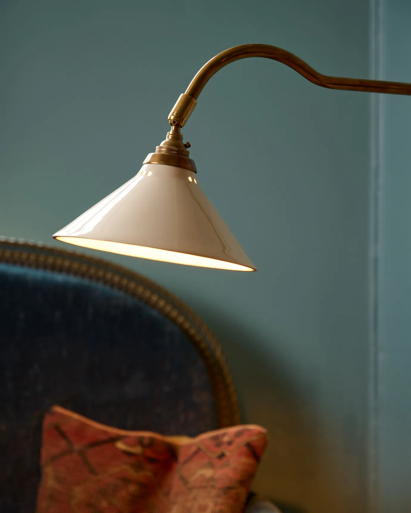 A close-up view of a small cream glazed ceramic light shade fitted to a curved brass arm.