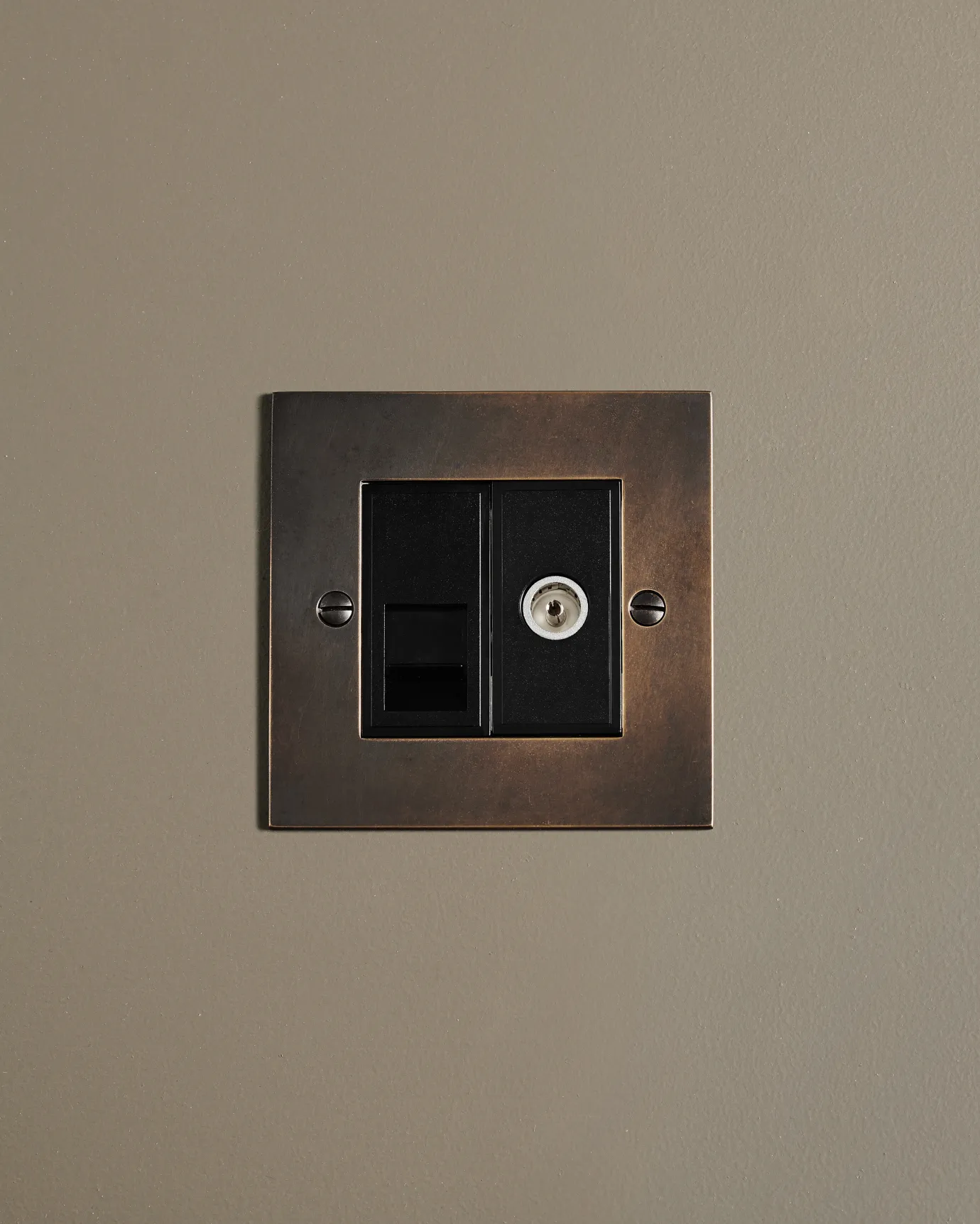 A straight-on view of a classic mixed telecom and coaxial TV socket in a dark oxidised brass finish.