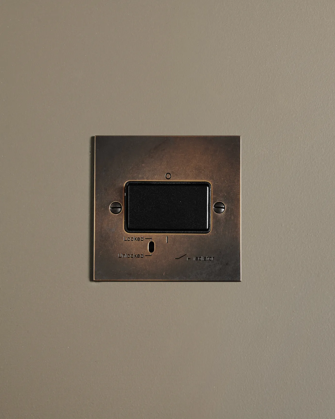 A straight-on view of a classic extractor fan isolator switch a dark oxidised brass finish.