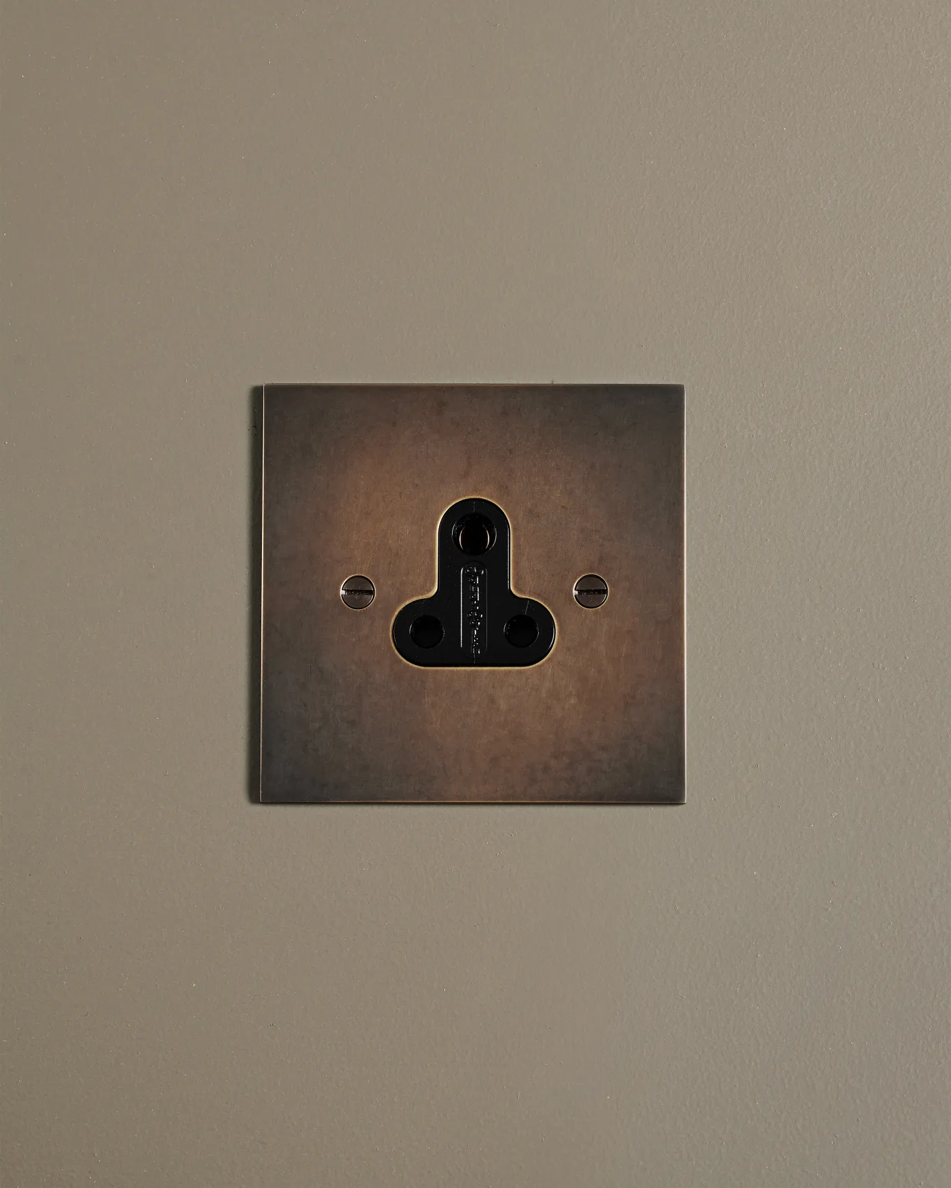 A straight-on view of a classic 5 amp single plug socket in a dark oxidised brass finish.