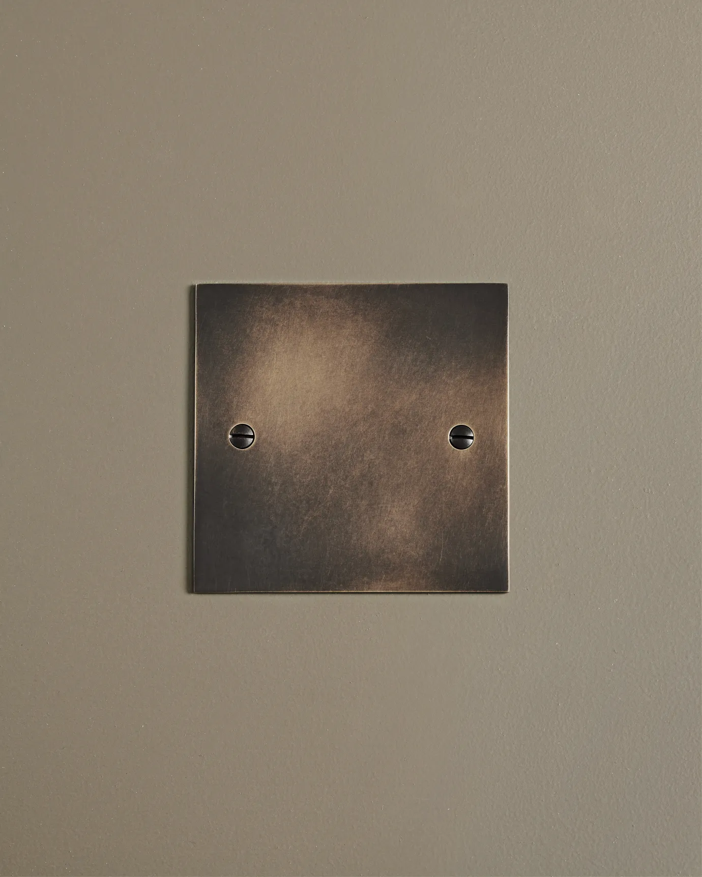 A straight-on view of a classic blank socket plate in a dark oxidised brass finish.