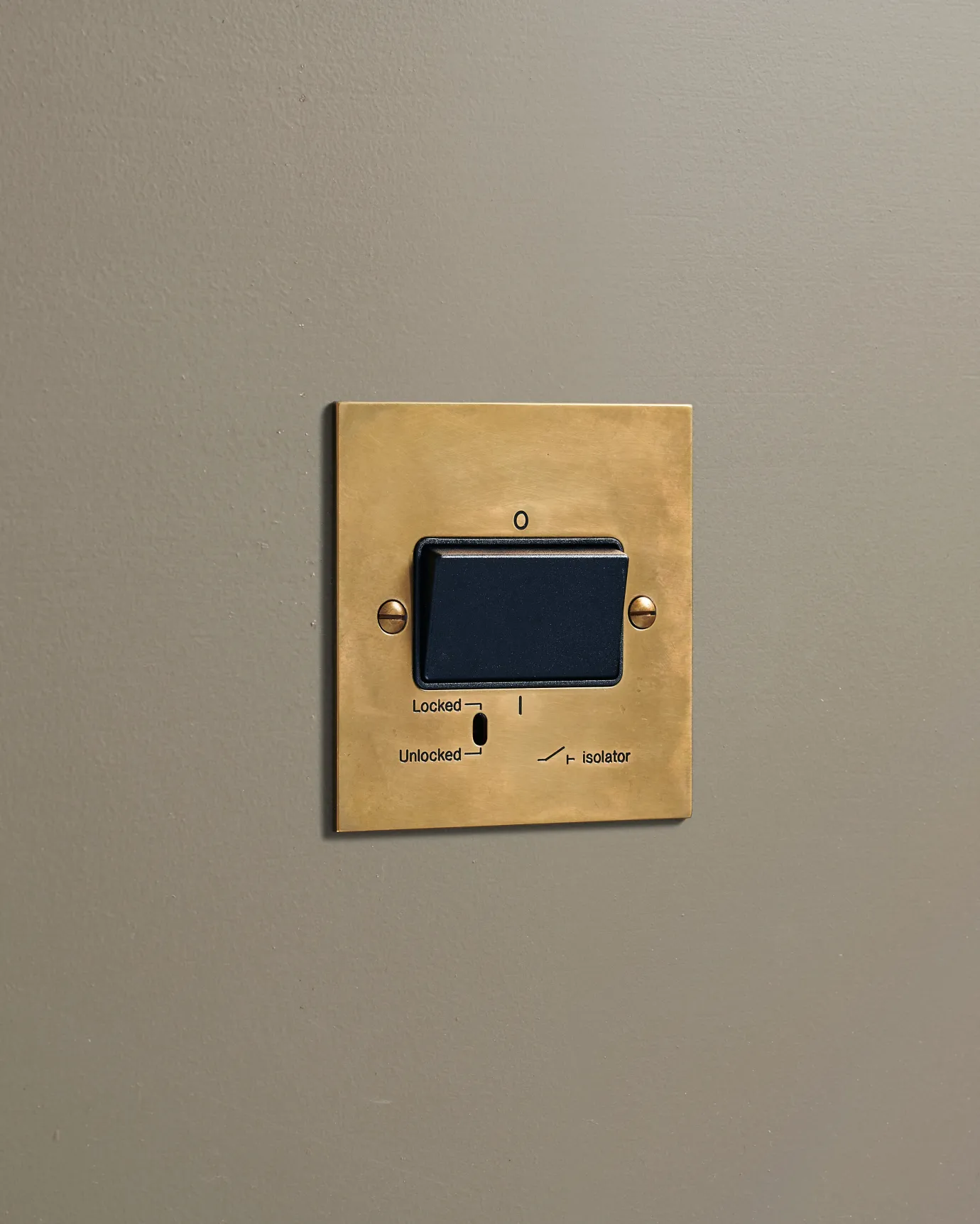 An oblique view of a classic extractor fan isolator switch in a warm burnished brass finish.