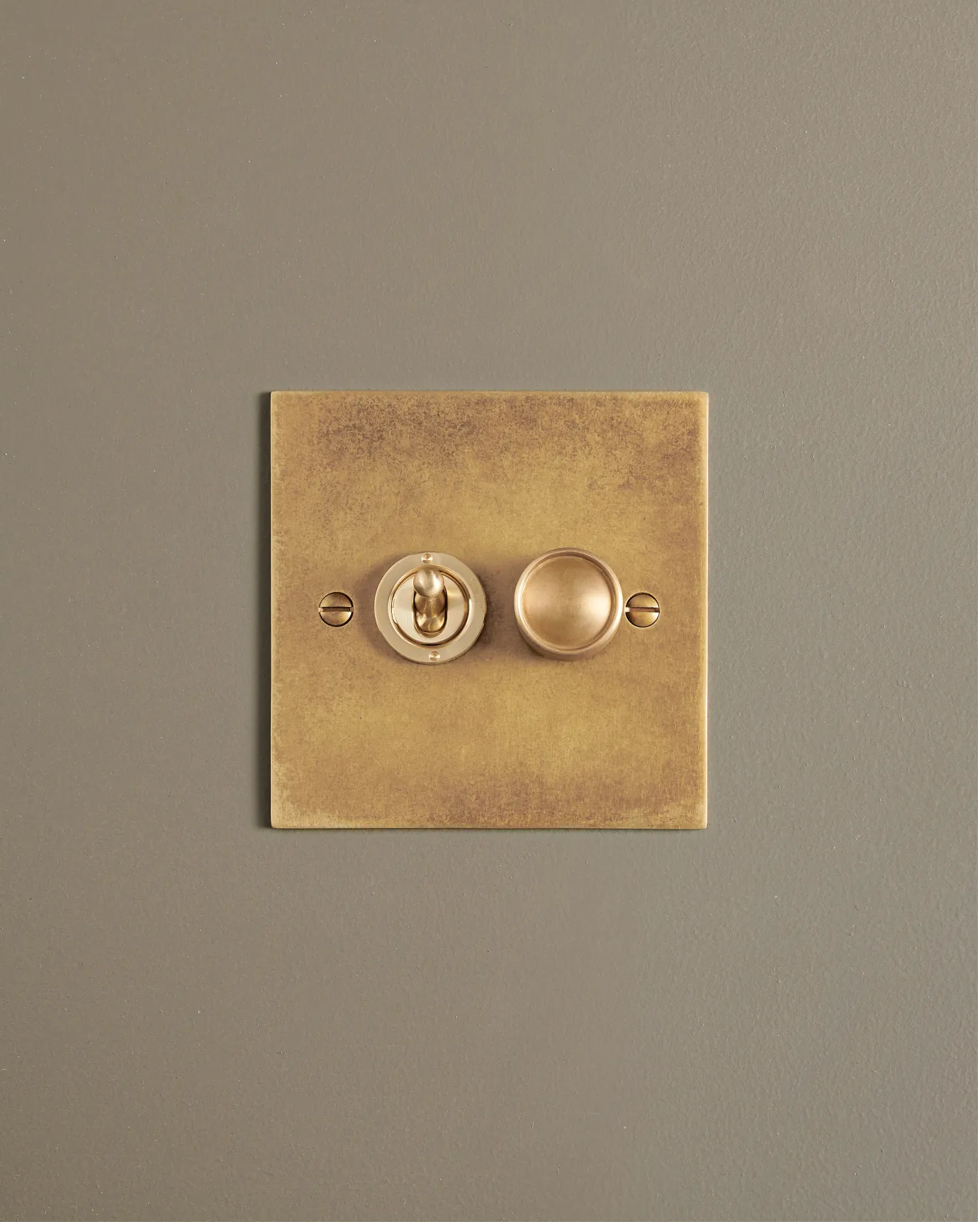 A straight-on view of a 2 gang classic toggle and dimmer mixed switch in a mottled aged brass finish.