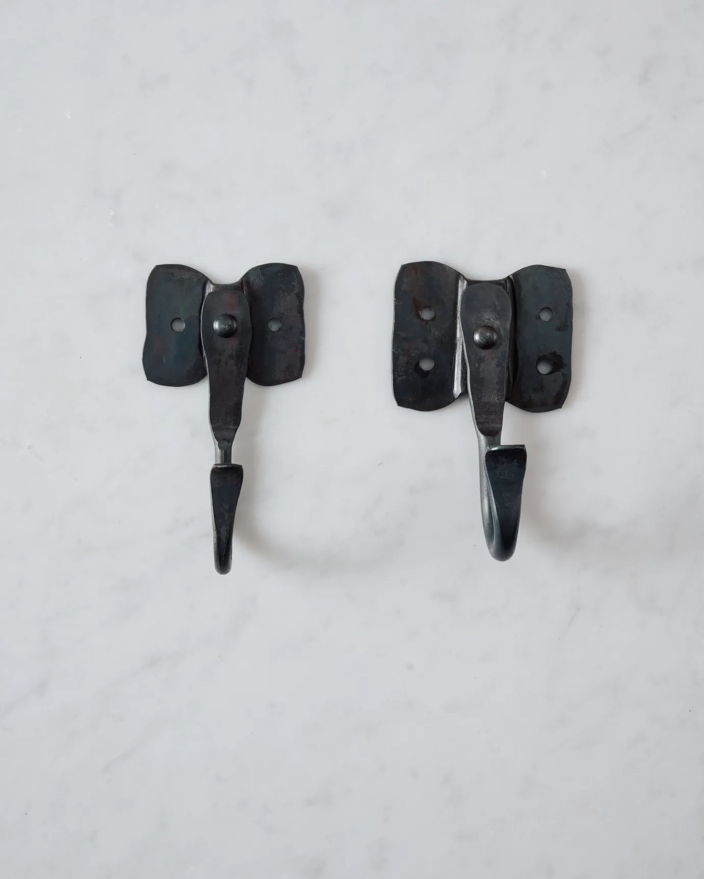 Two iron wall hooks with backplates shaped like elephant ears, one small and one large.