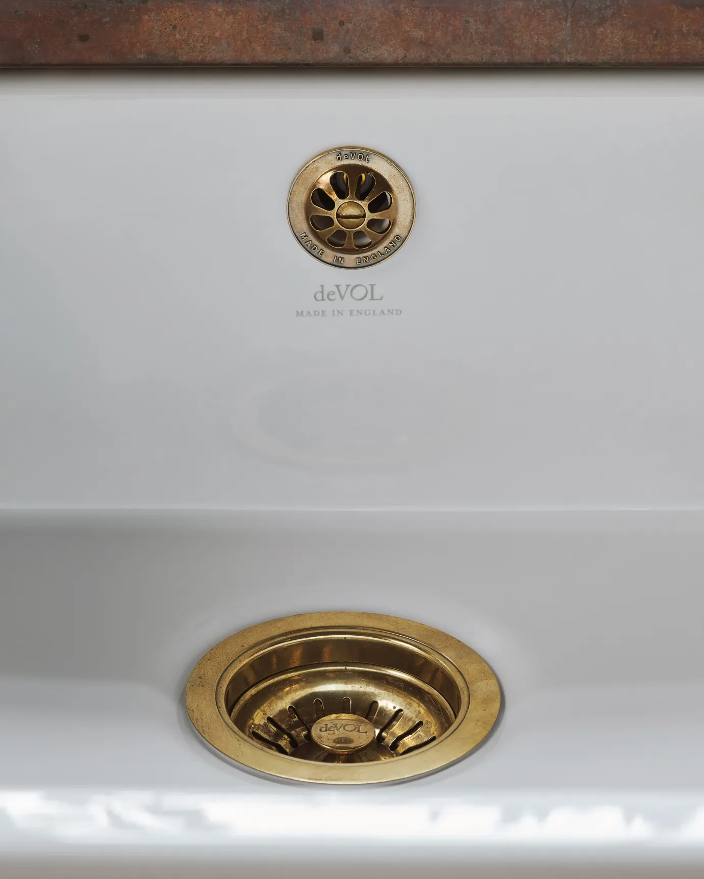 A straight-on view of a basket waste strainer with a deVOL domed overflow cap in a warm burnished brass finish, there is a small 'deVOL' logo in the middle of the waste strainer finial.