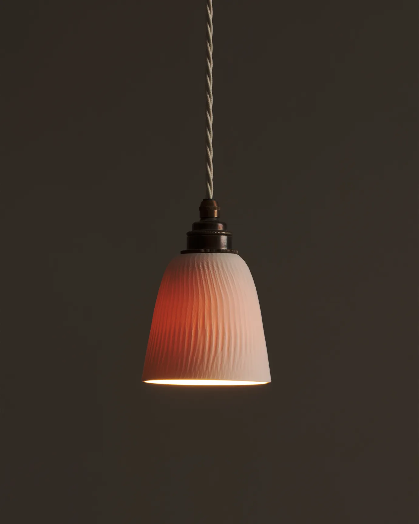 A large chattered beaker porcelain pendant with the light on, showing the warm red glow of the translucent surface.