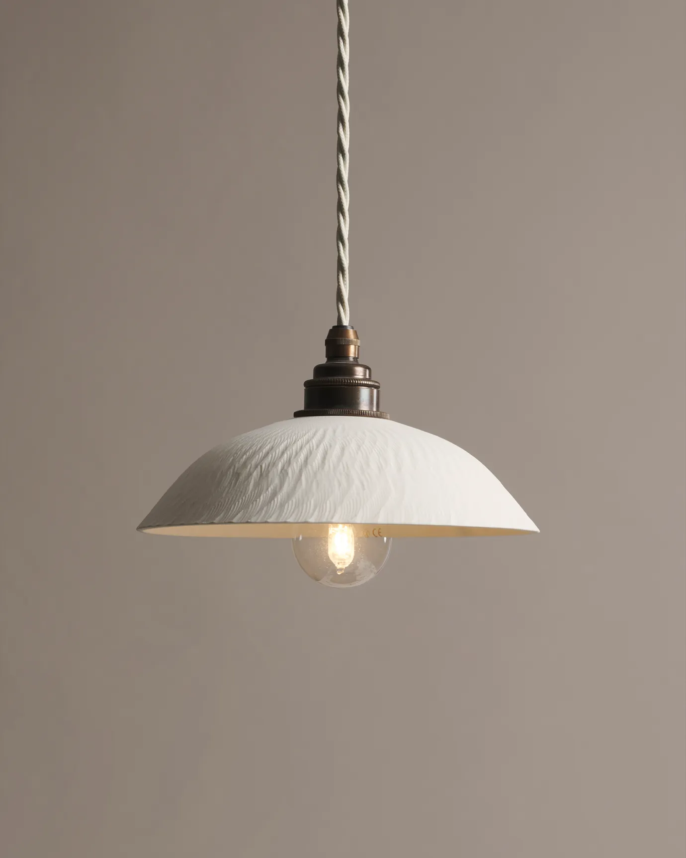 A large chattered skullcap porcelain pendant light with an unglazed finish, an aged brass E27 lampholder and a white twisted fabric flex cord.