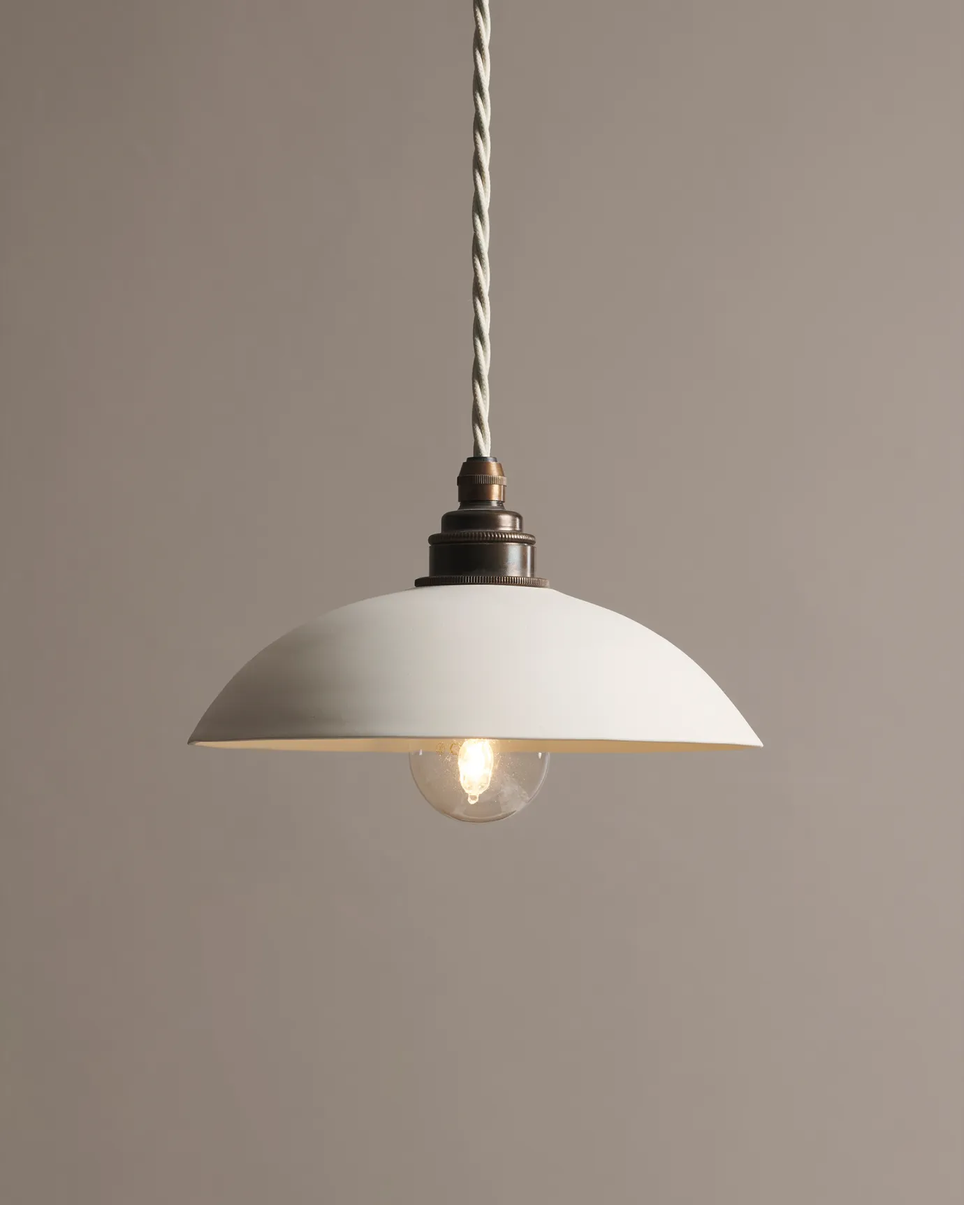 A large plain skullcap porcelain pendant light with an unglazed finish, an aged brass E27 lampholder and a white twisted fabric flex cord.