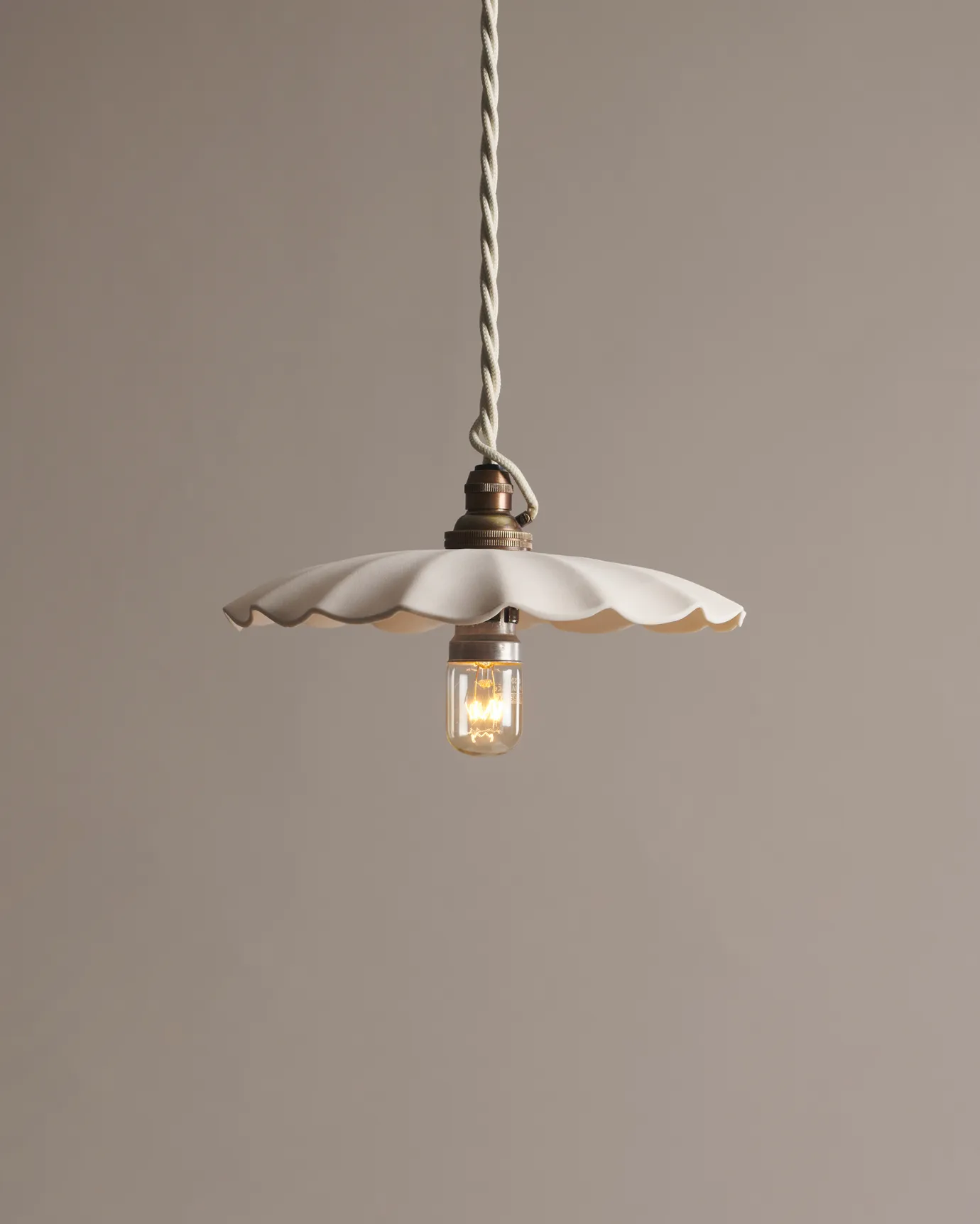 A large wide pleat porcelain pendant light with an unglazed finish, an aged brass B22 lampholder and a white twisted fabric flex cord.