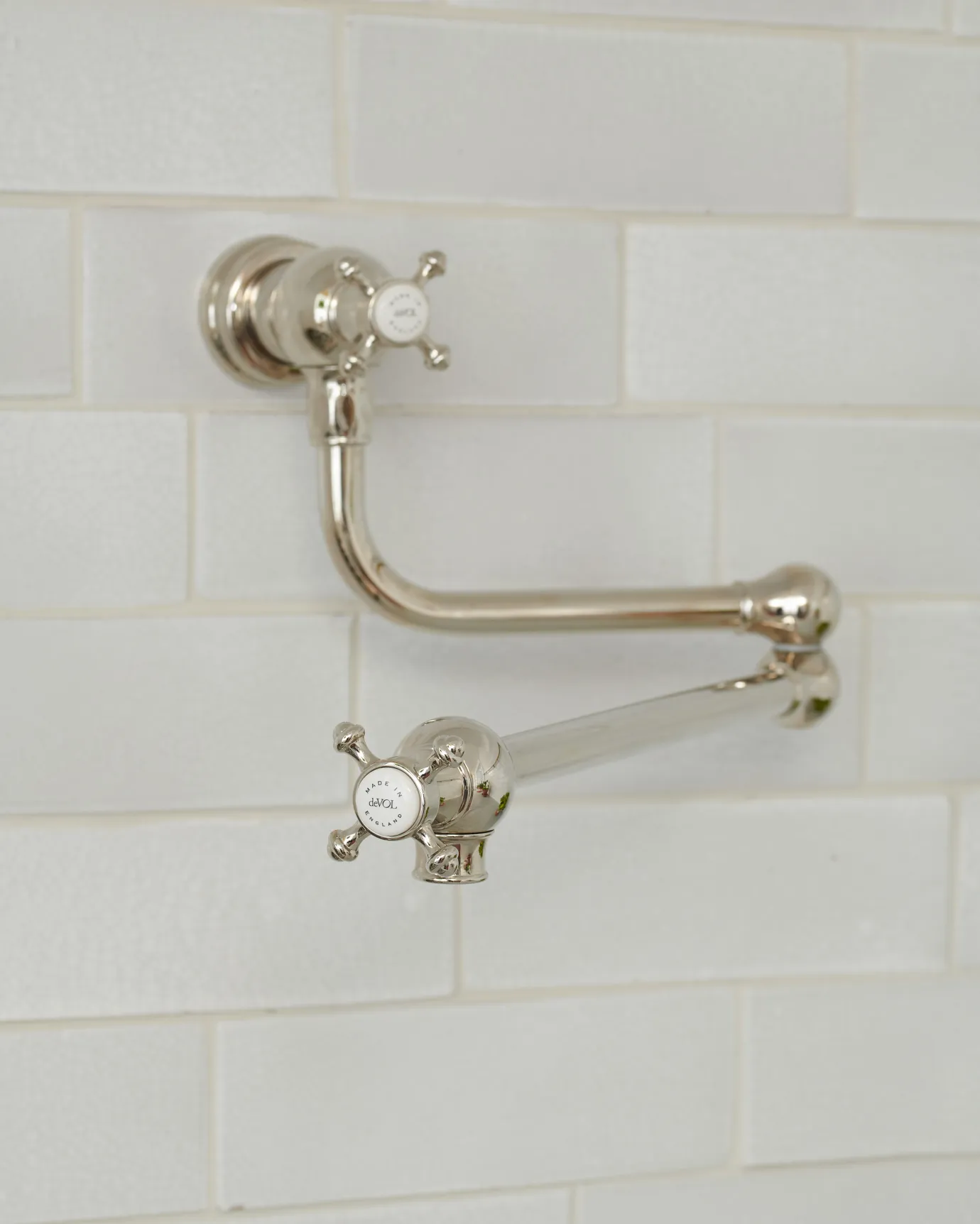 An oblique view of a traditional-style nickel pot filler tap with crosshead handles fitted to a wall of white metro tiles.