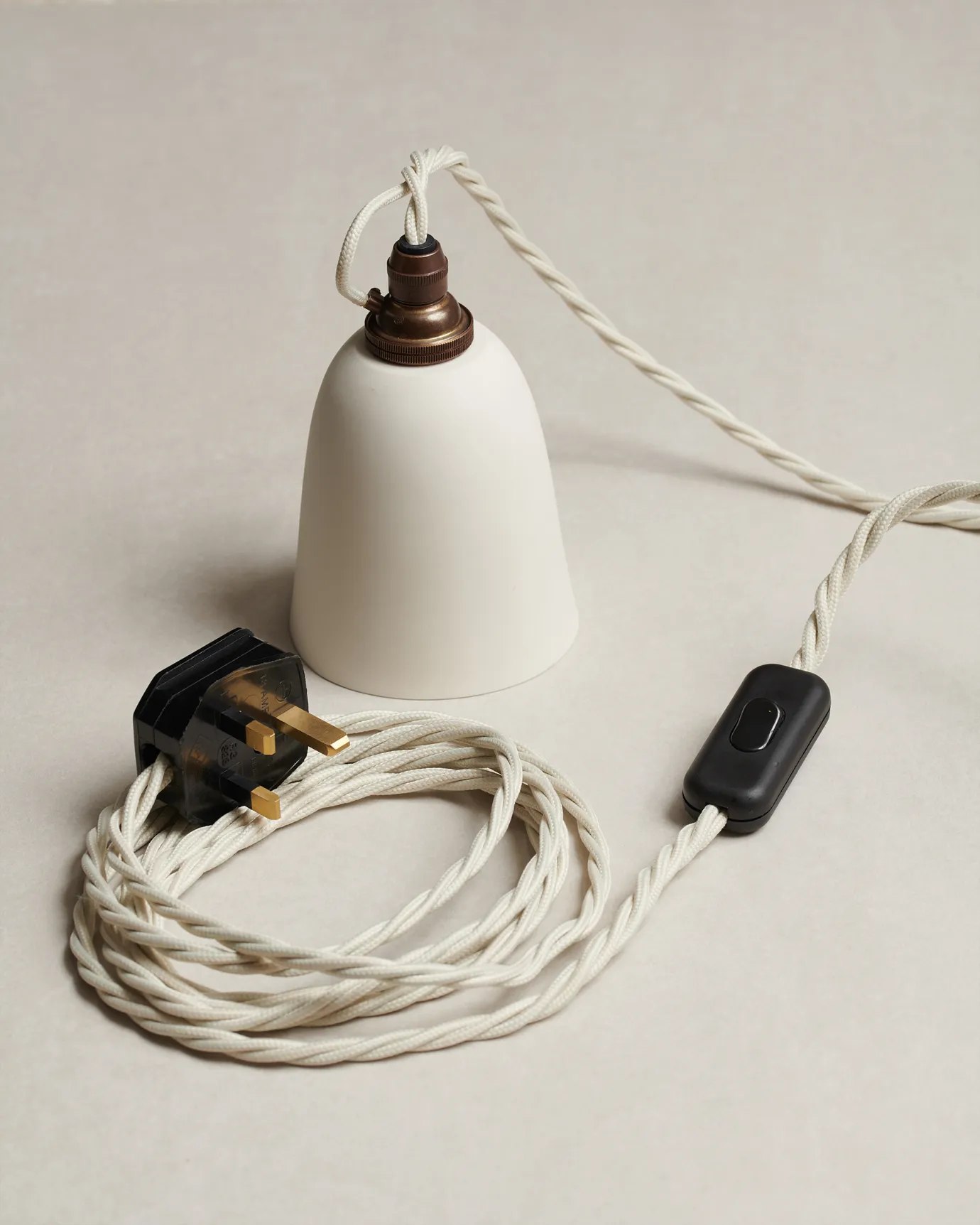 A small plain beaker porcelain plug-in light with an unglazed finish, white twisted fabric flex cord, brass fittings and a black plastic switch and plug.