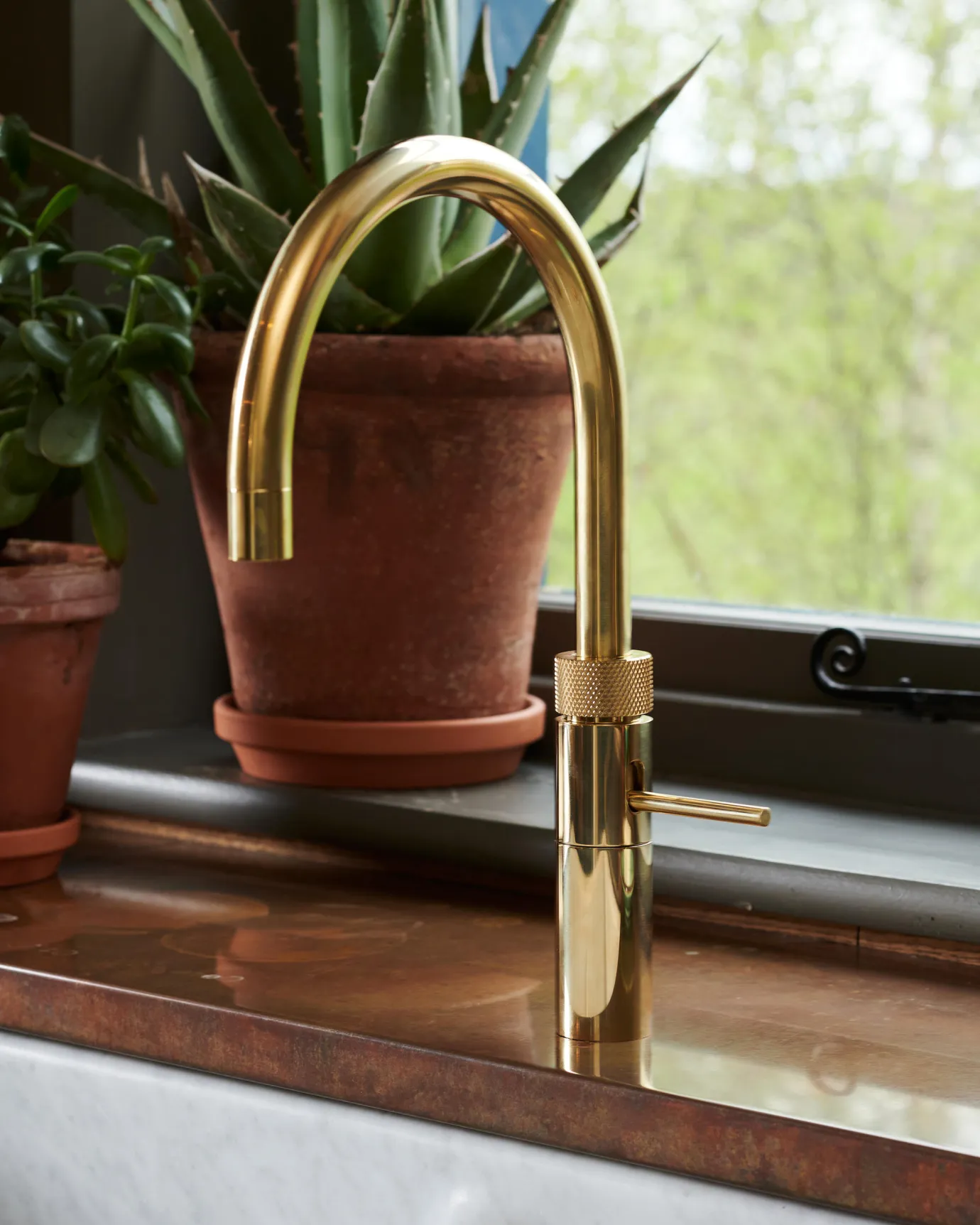 A contemporary-style brass tap with a small lever handle and a minimal design on an aged copper worktop.