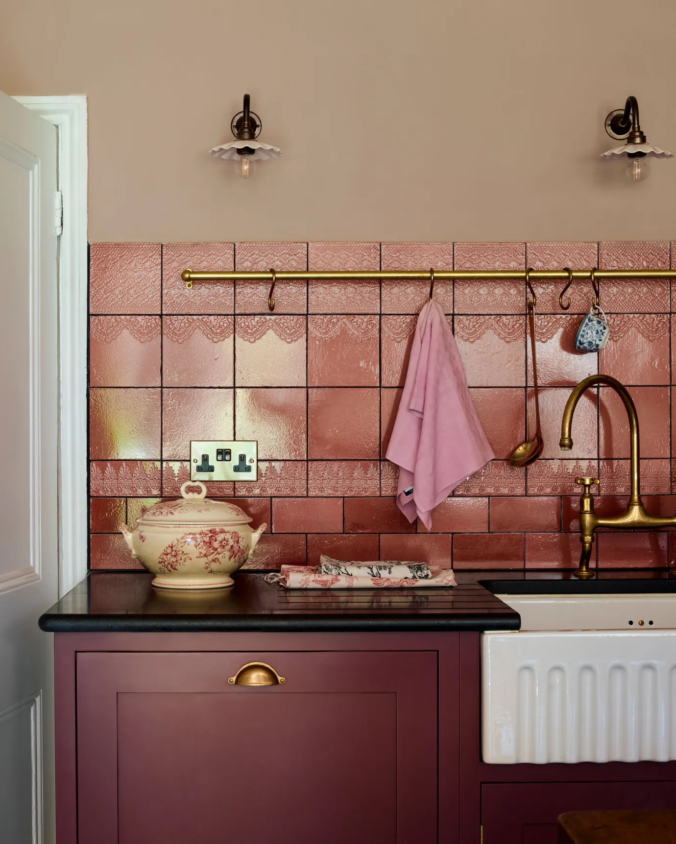 A red painted Shaker kitchen with our glossy 'Lace Market Tiles' in a rich rose colour, complemented by aged brass hanging rails for holding cooking utensils and tea towels.