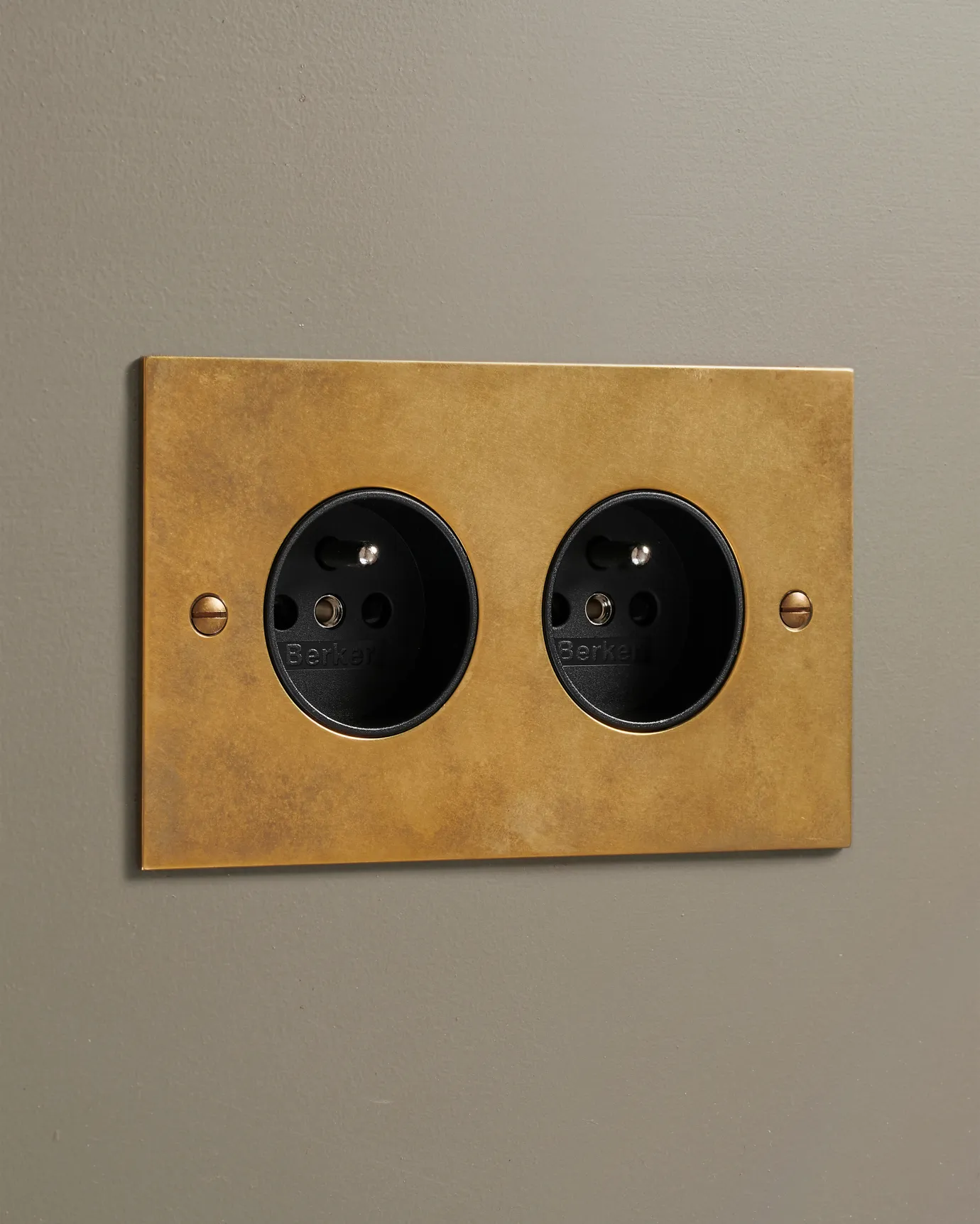 An oblique view of a classic French-style twin plug socket in a warm burnished brass finish.