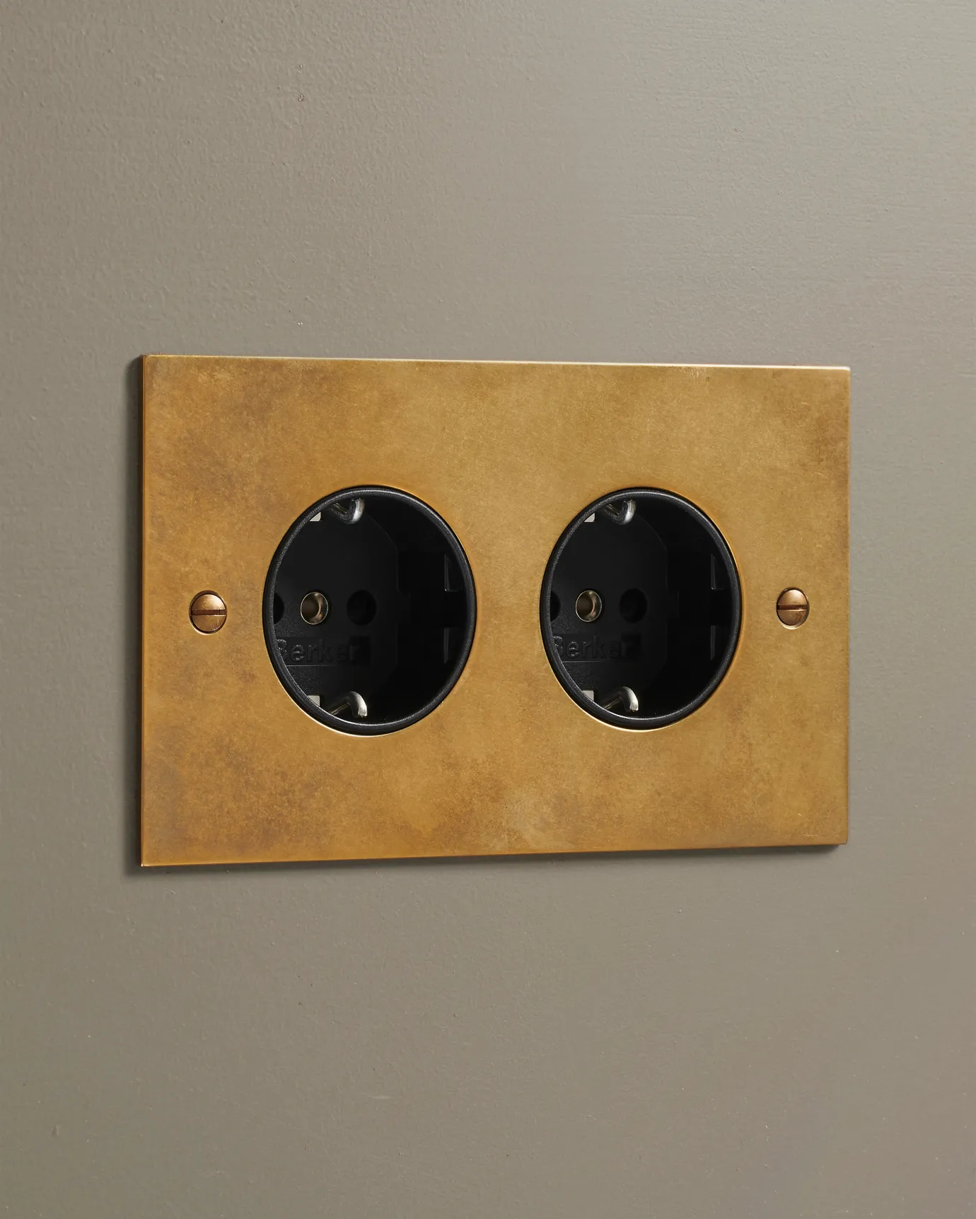 An oblique view of a classic Schuko-style twin plug socket in a warm burnished brass finish.