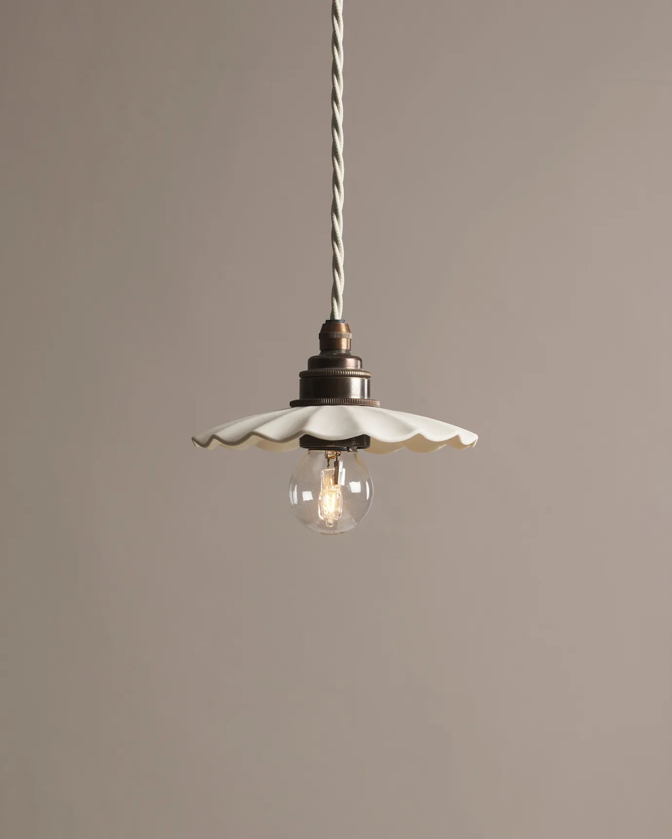 A small wide pleat porcelain pendant light with an unglazed finish, an aged brass E27 lampholder and a white twisted fabric flex cord.