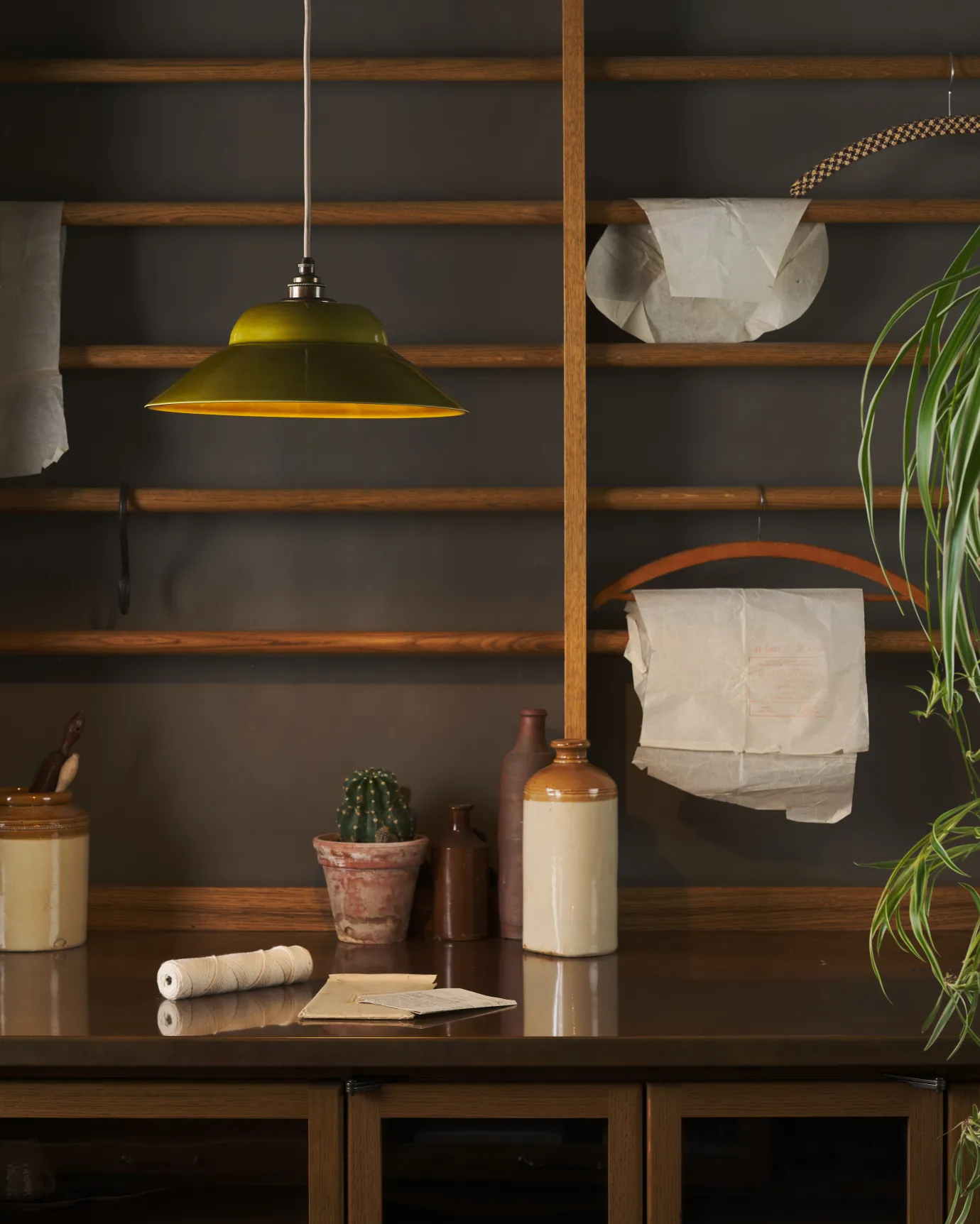 A straight-on view of a mid-century-style chartreuse glazed ceramic pendant light in front of oak racking.