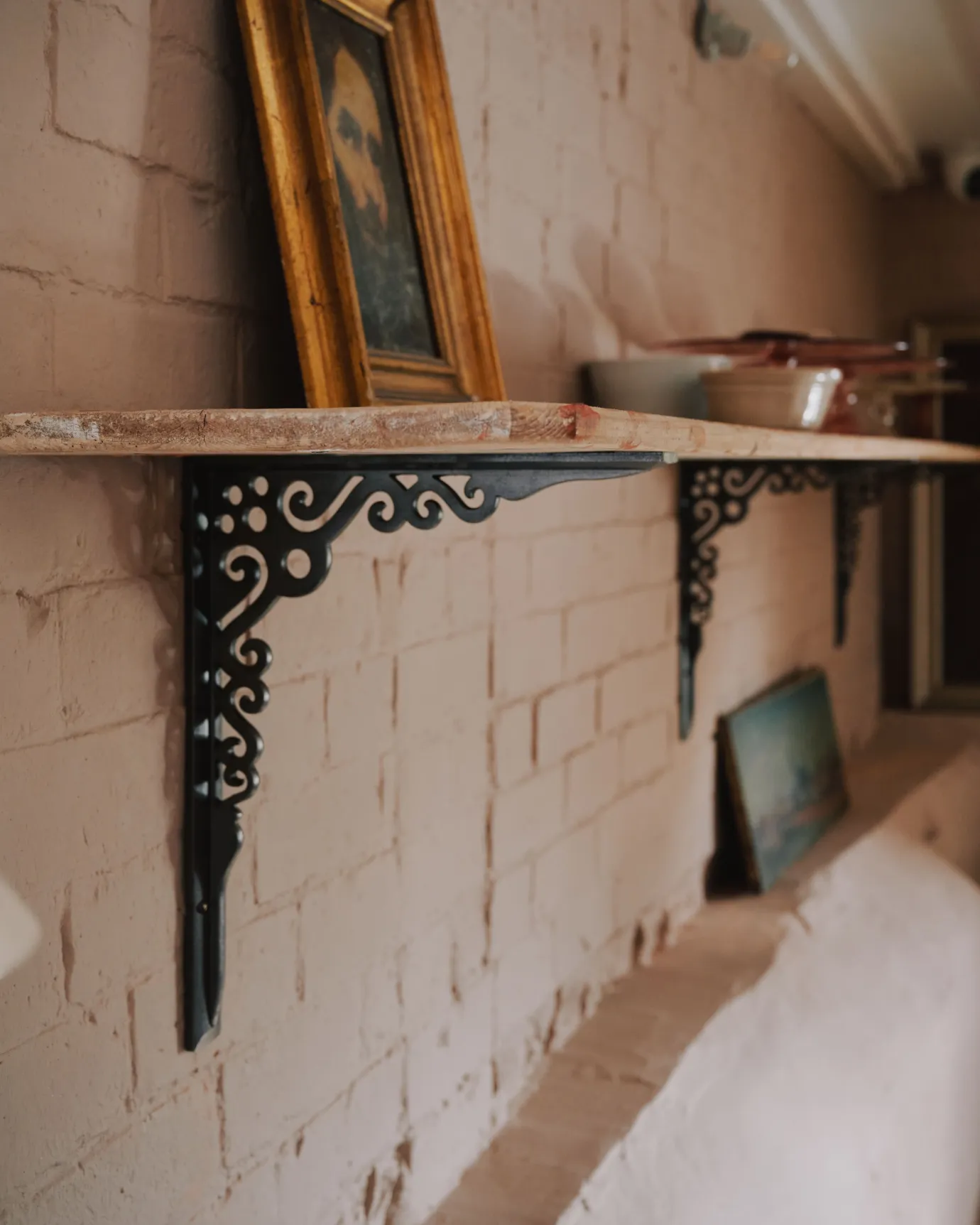 An oblique view of a large Victorian-inspired ornate cast iron shelf bracket holding a deep pine shelf to a pink colour brick wall.